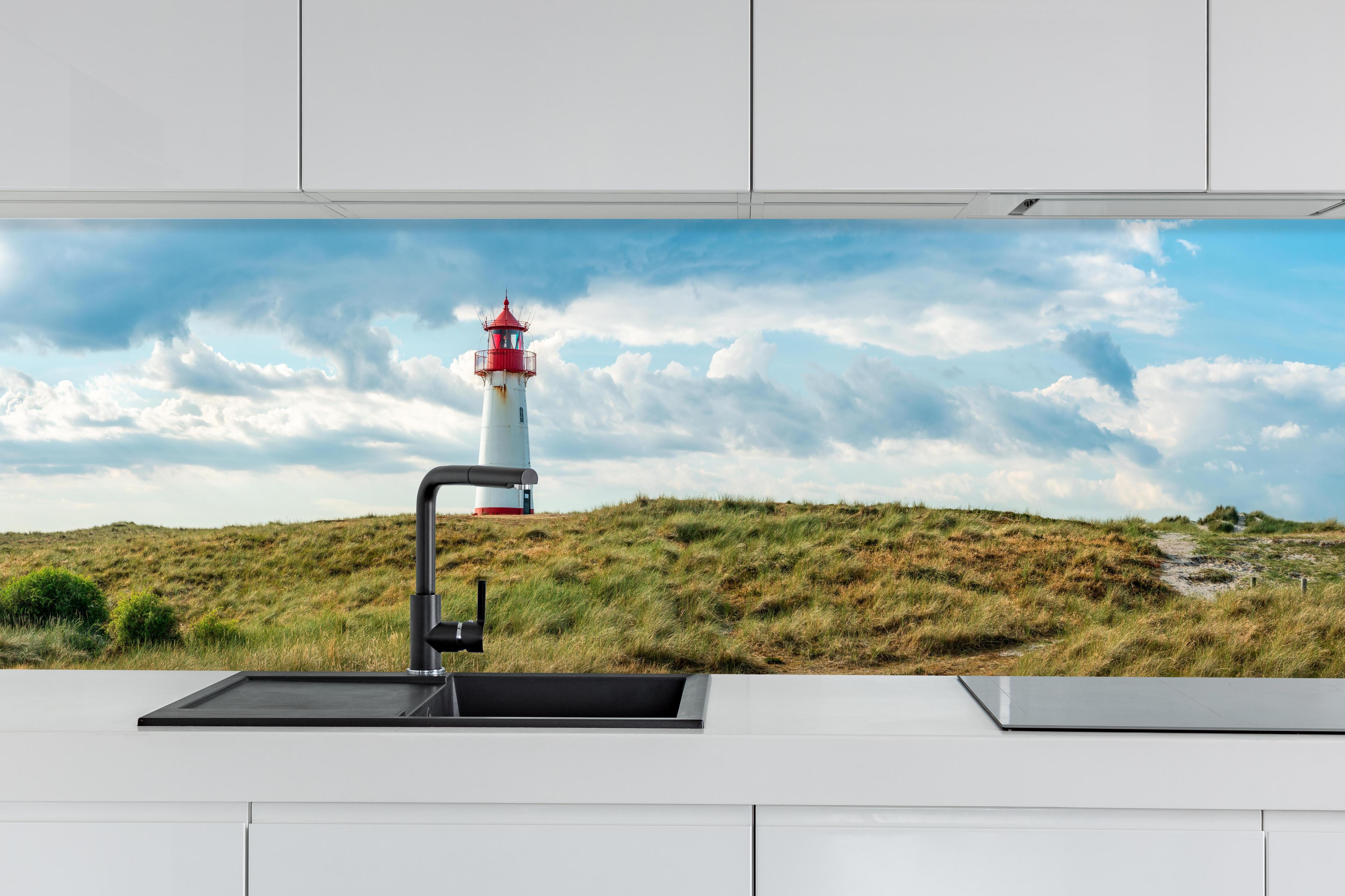 Küche - Idyllischer Leuchtturm umgeben von weiten Grasfeldern hinter weißen Hochglanz-Küchenregalen und schwarzem Wasserhahn