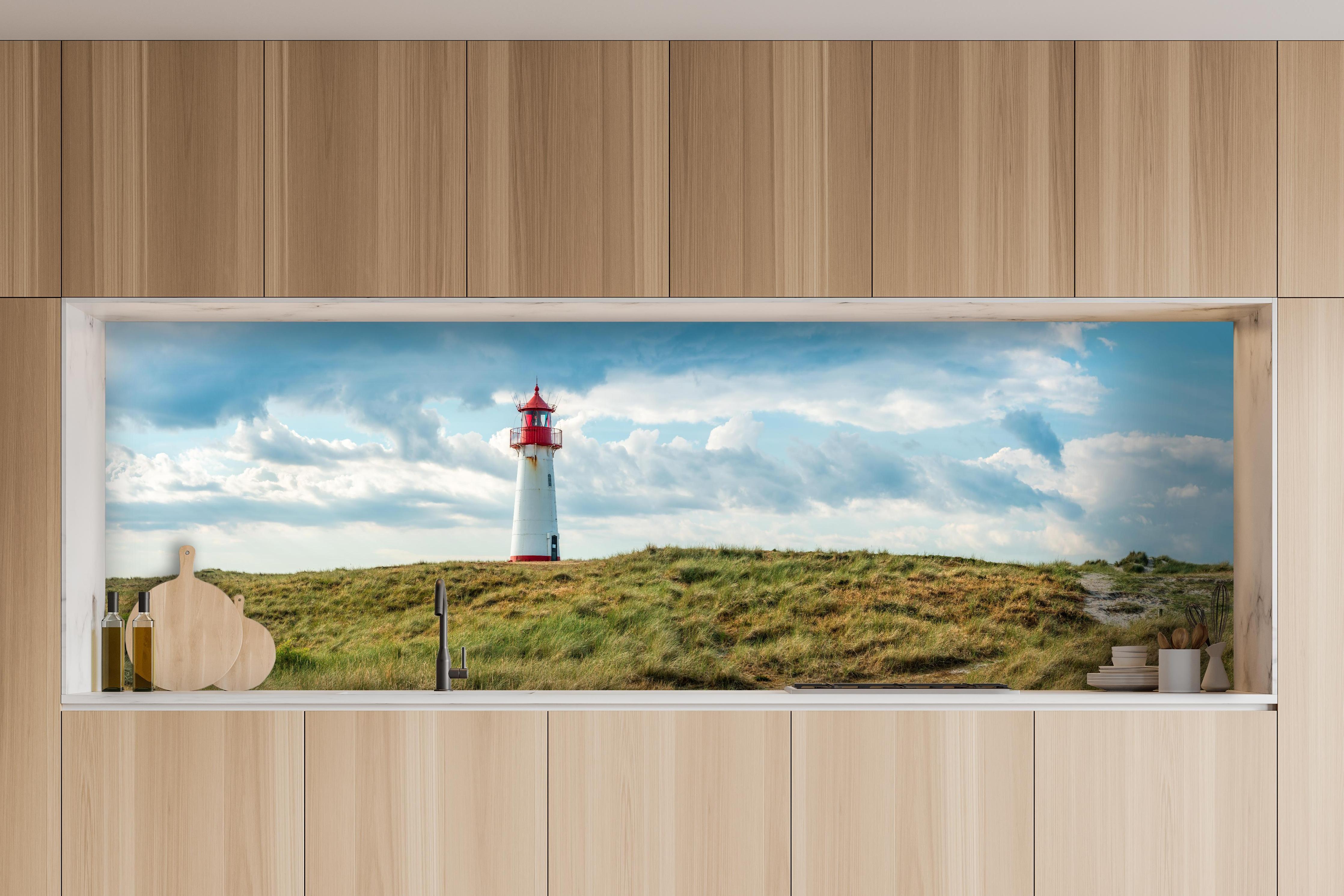 Küche - Idyllischer Leuchtturm umgeben von weiten Grasfeldern hinter weißen Hochglanz-Küchenregalen und schwarzem Wasserhahn