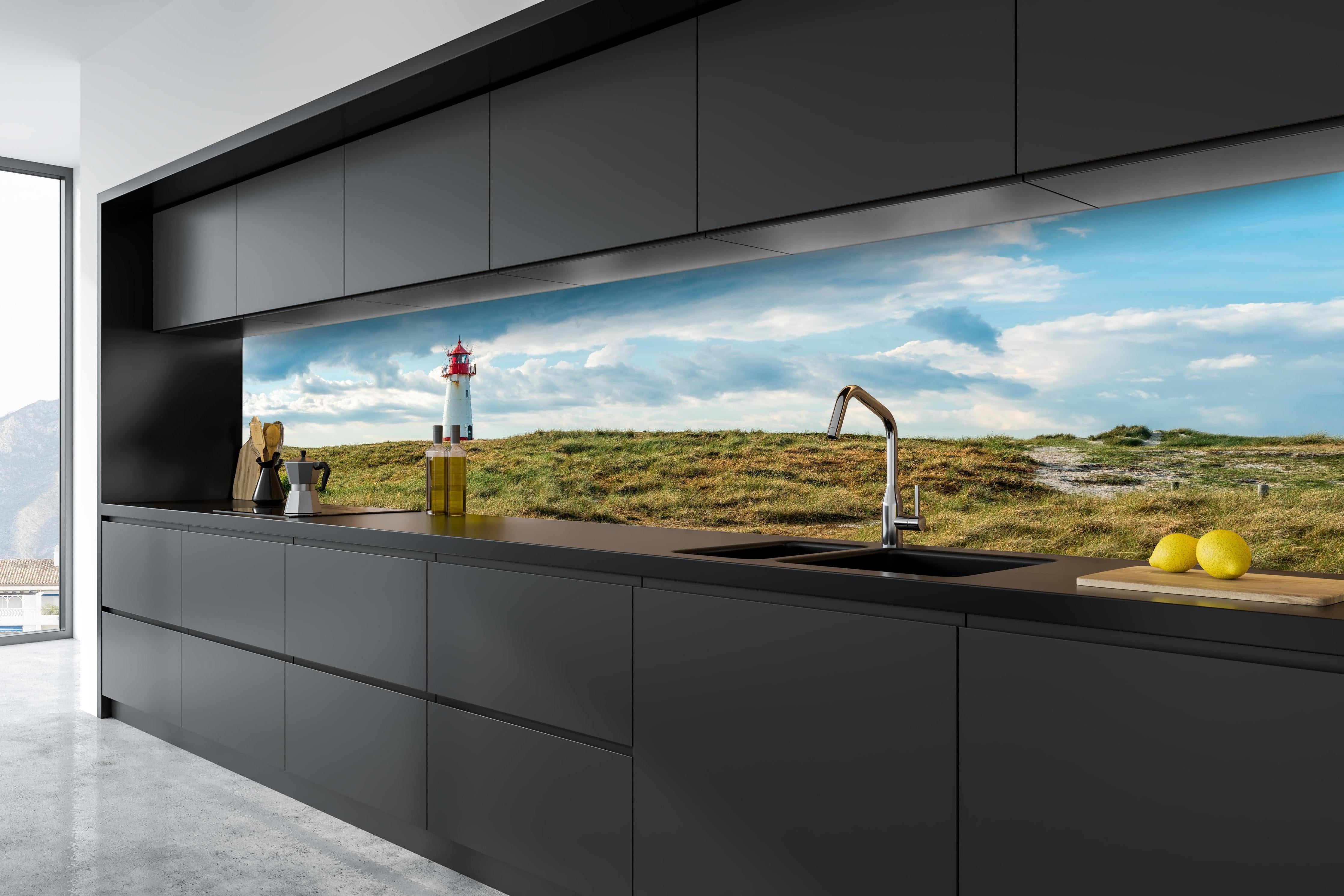Küche - Idyllischer Leuchtturm umgeben von weiten Grasfeldern hinter weißen Hochglanz-Küchenregalen und schwarzem Wasserhahn