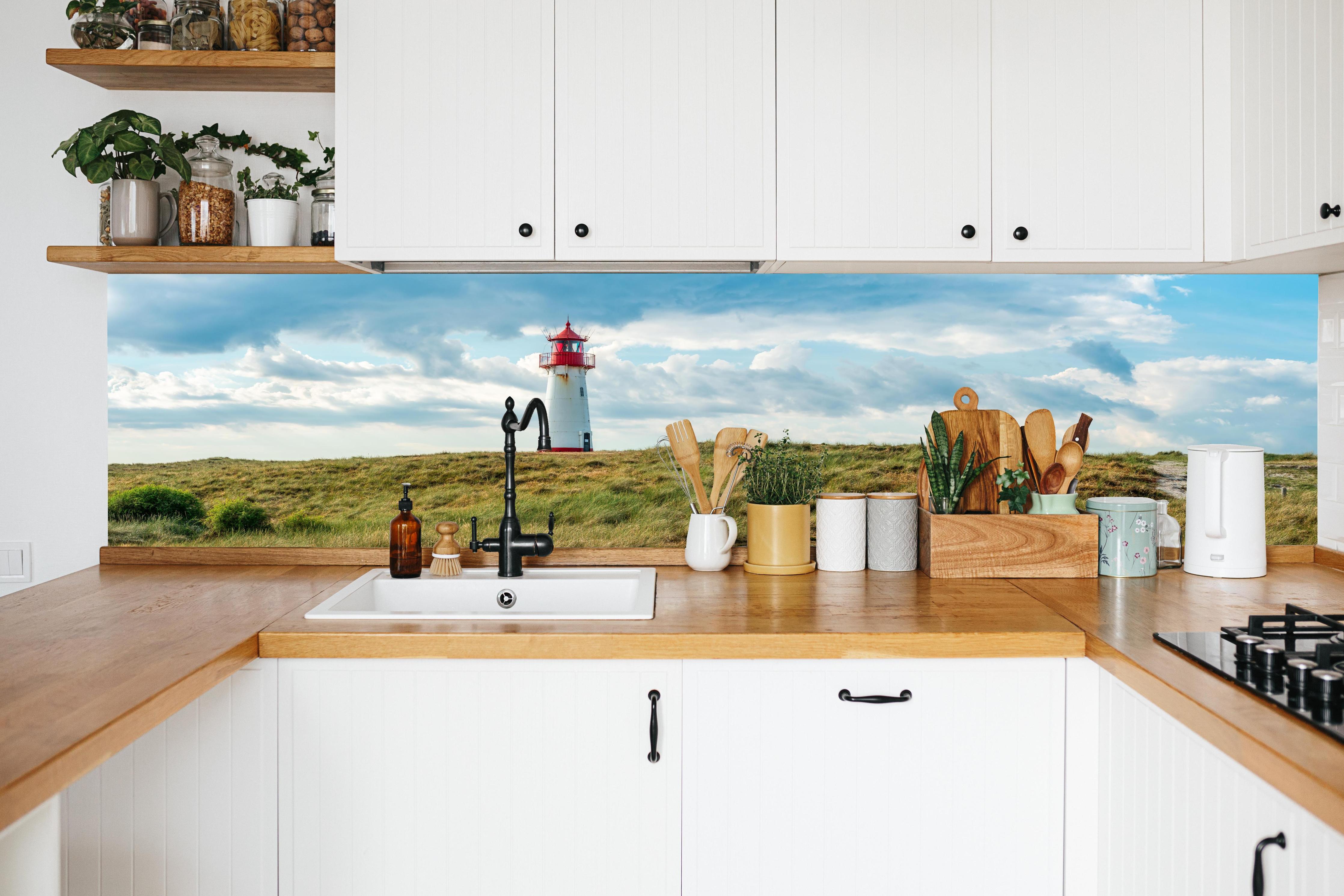 Küche - Idyllischer Leuchtturm umgeben von weiten Grasfeldern hinter weißen Hochglanz-Küchenregalen und schwarzem Wasserhahn