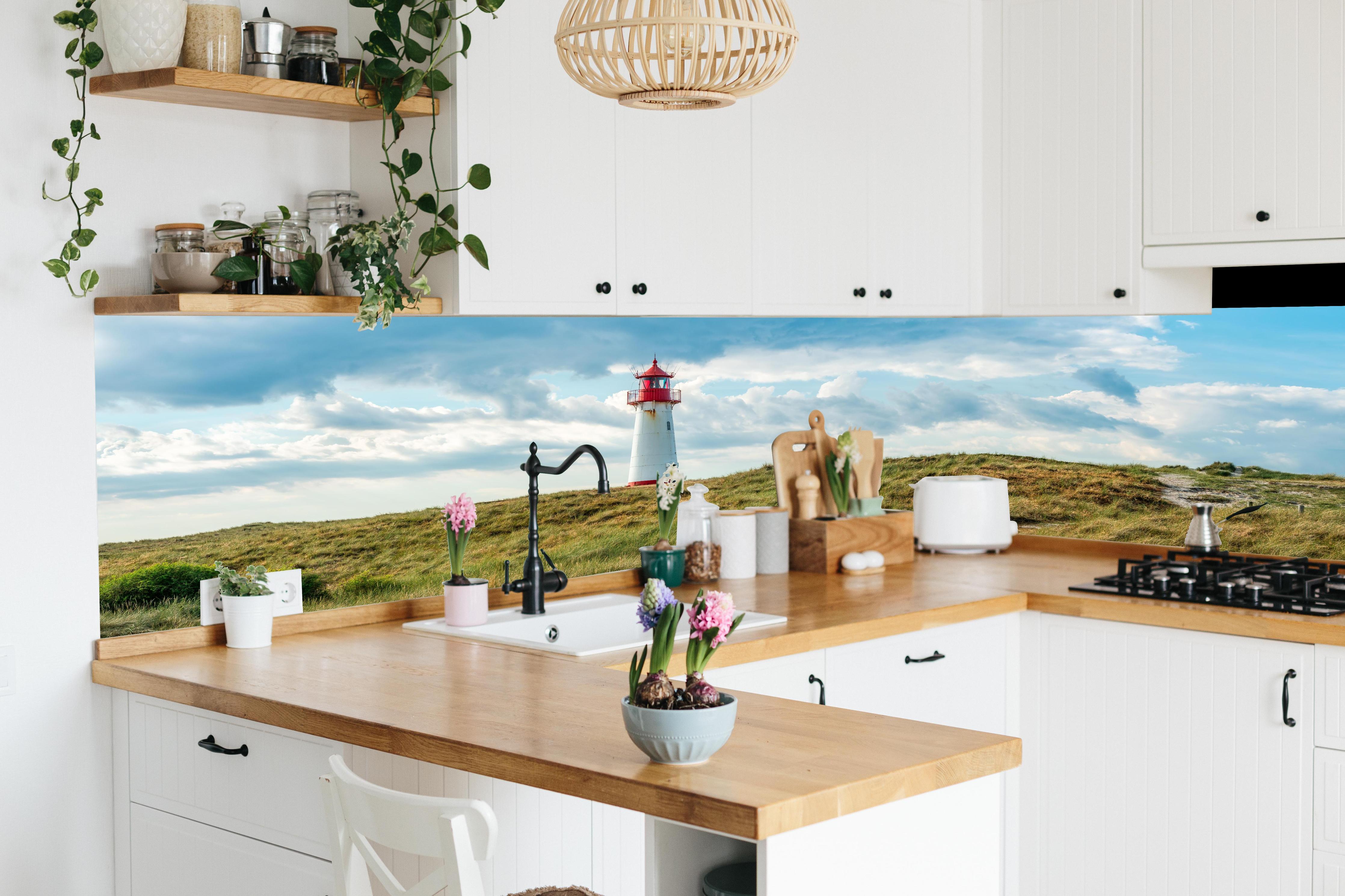 Küche - Idyllischer Leuchtturm umgeben von weiten Grasfeldern hinter weißen Hochglanz-Küchenregalen und schwarzem Wasserhahn