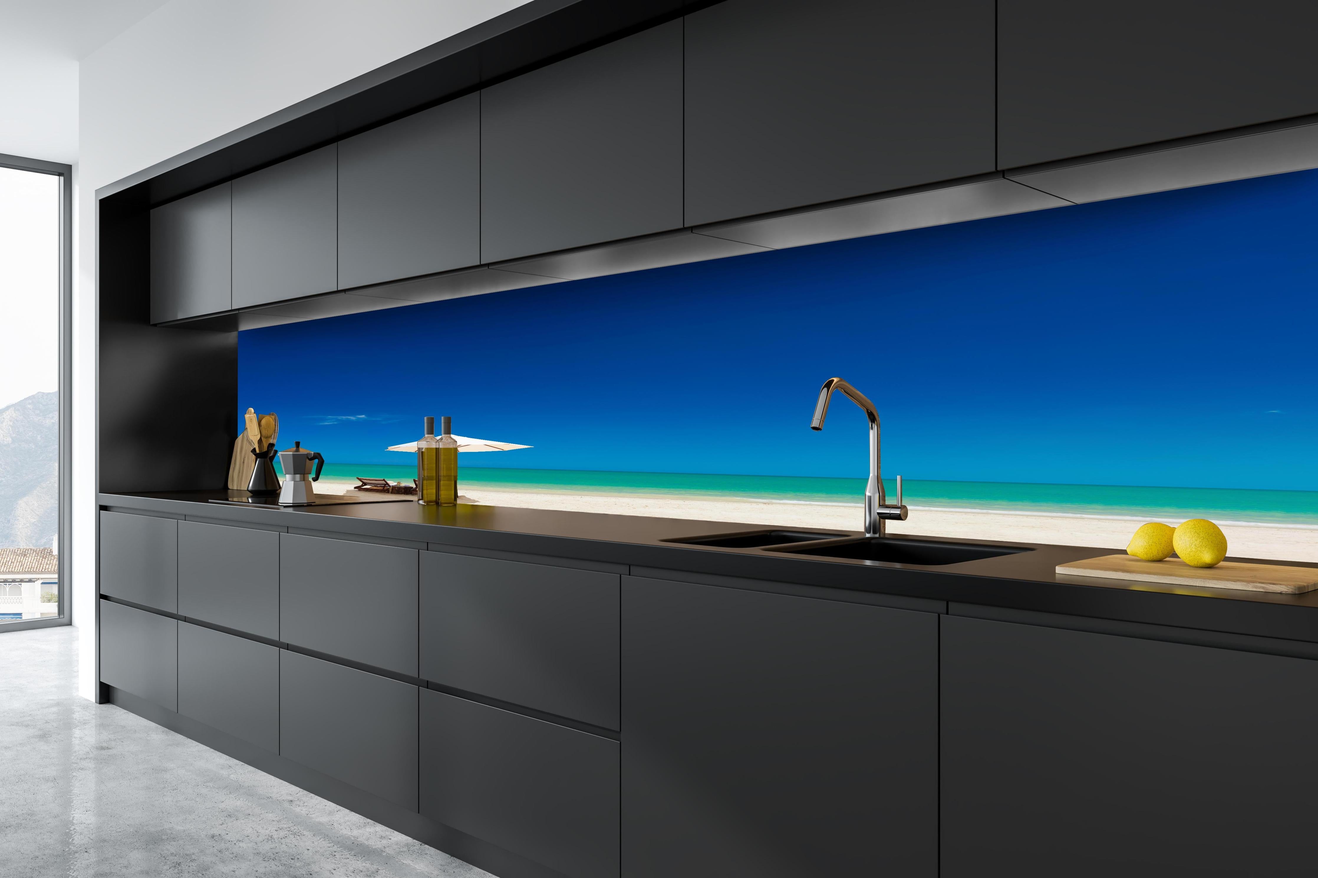 Küche - Idyllischer Strand mit Liegen und Sonnenschirm unter blauem Himmel hinter weißen Hochglanz-Küchenregalen und schwarzem Wasserhahn