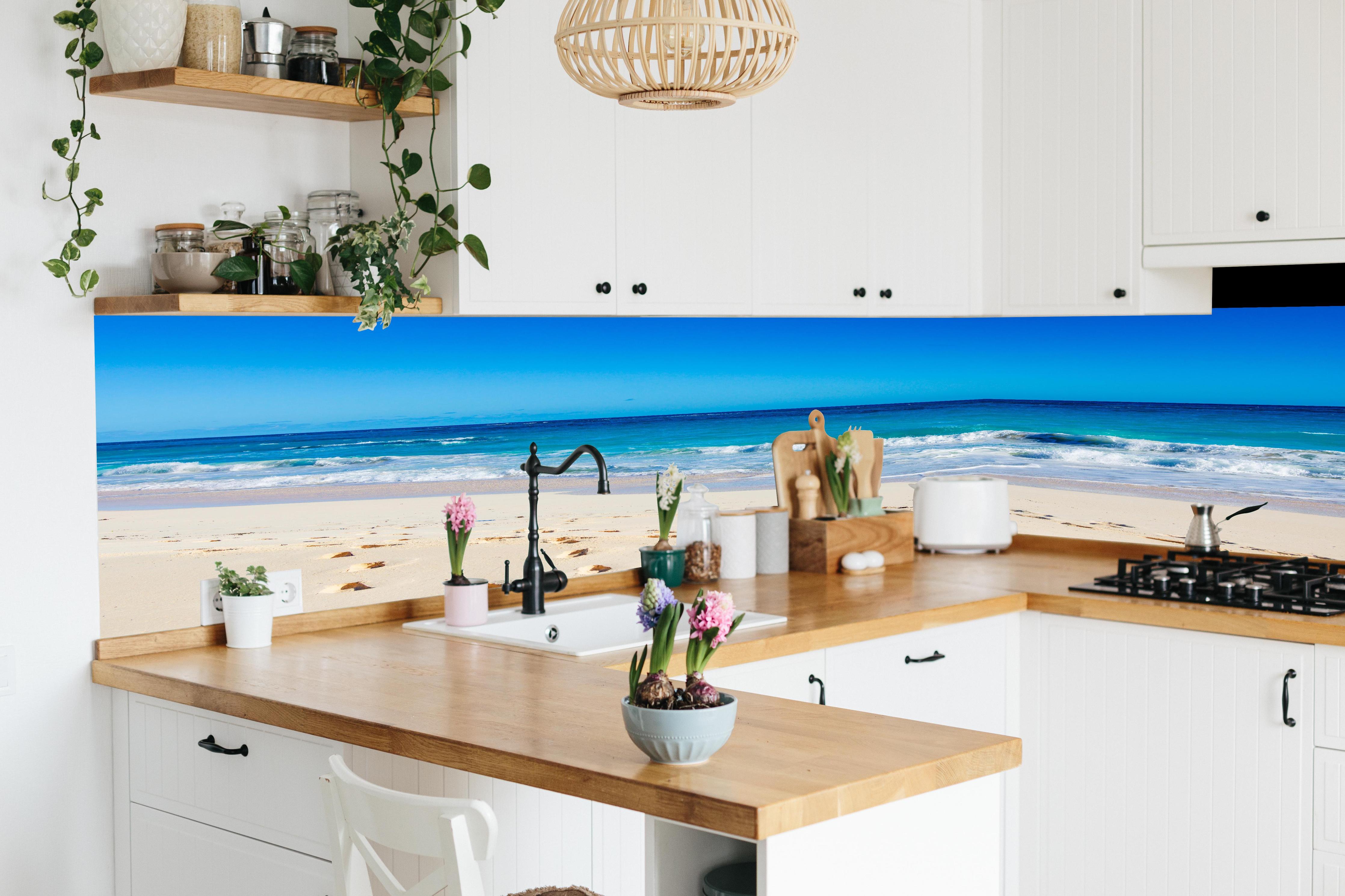 Küche - Idyllischer Strand mit feinem Sand und türkisfarbenem Wasser hinter weißen Hochglanz-Küchenregalen und schwarzem Wasserhahn