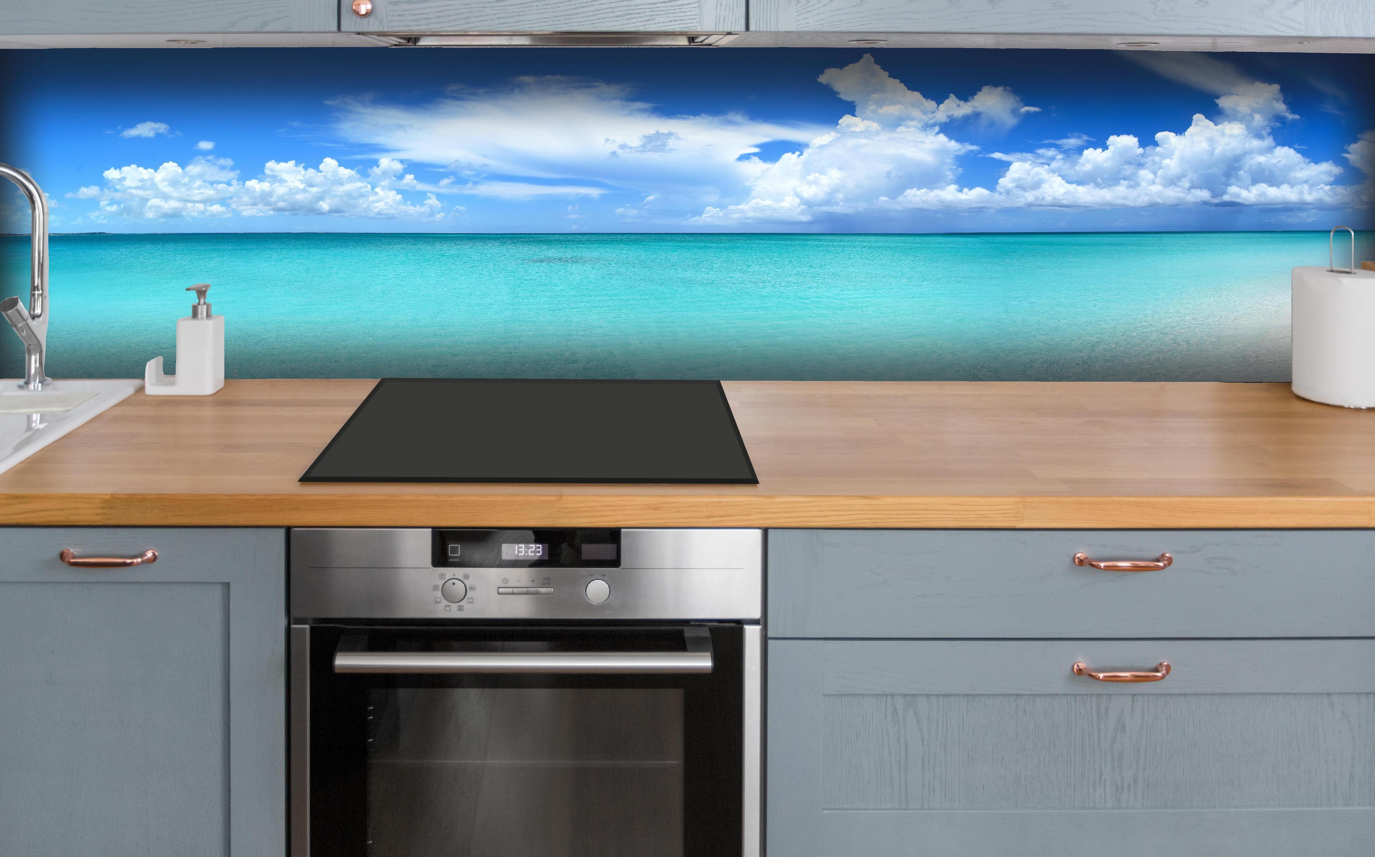 Küche - Idyllischer Strand unter einem strahlend blauen Himmel hinter weißen Hochglanz-Küchenregalen und schwarzem Wasserhahn