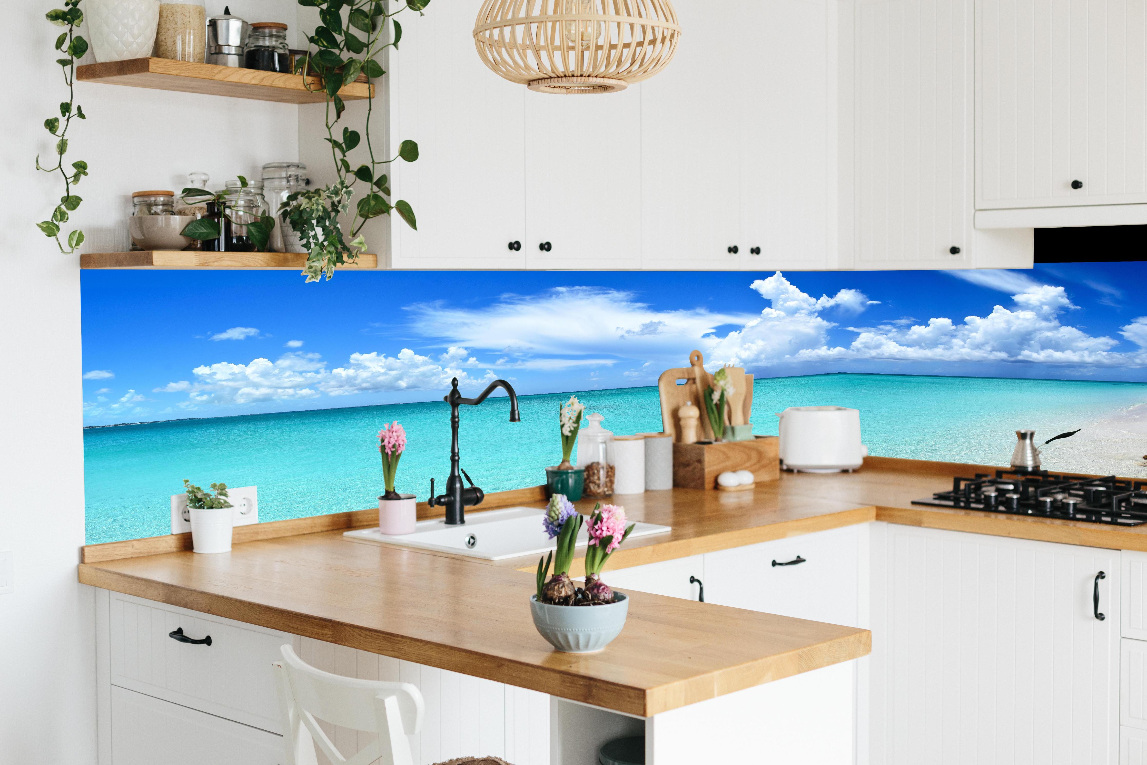 Küche - Idyllischer Strand unter einem strahlend blauen Himmel hinter weißen Hochglanz-Küchenregalen und schwarzem Wasserhahn