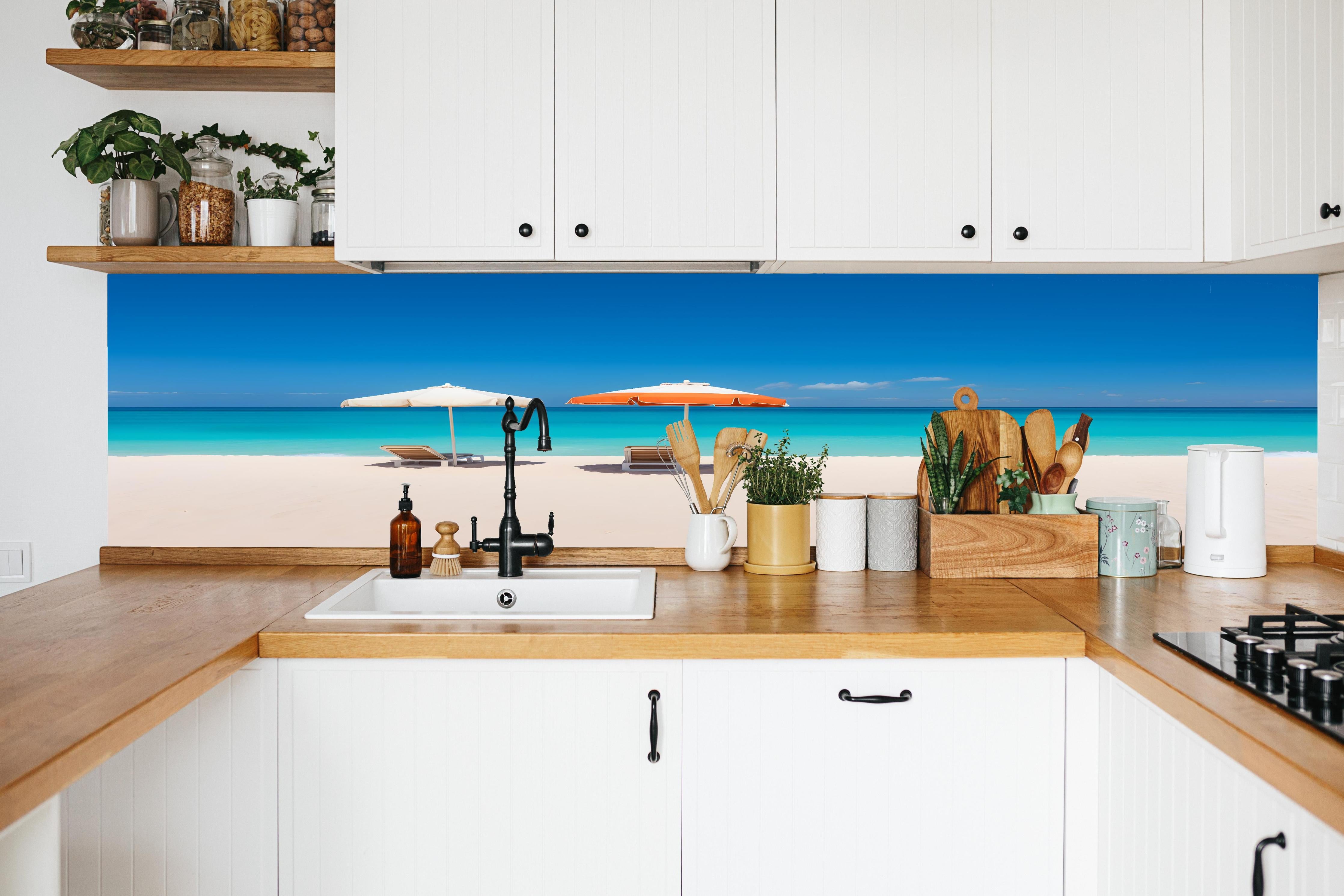 Küche - Idyllischer tropischer Strand mit weißen Sand und sonnigen Schirmen hinter weißen Hochglanz-Küchenregalen und schwarzem Wasserhahn