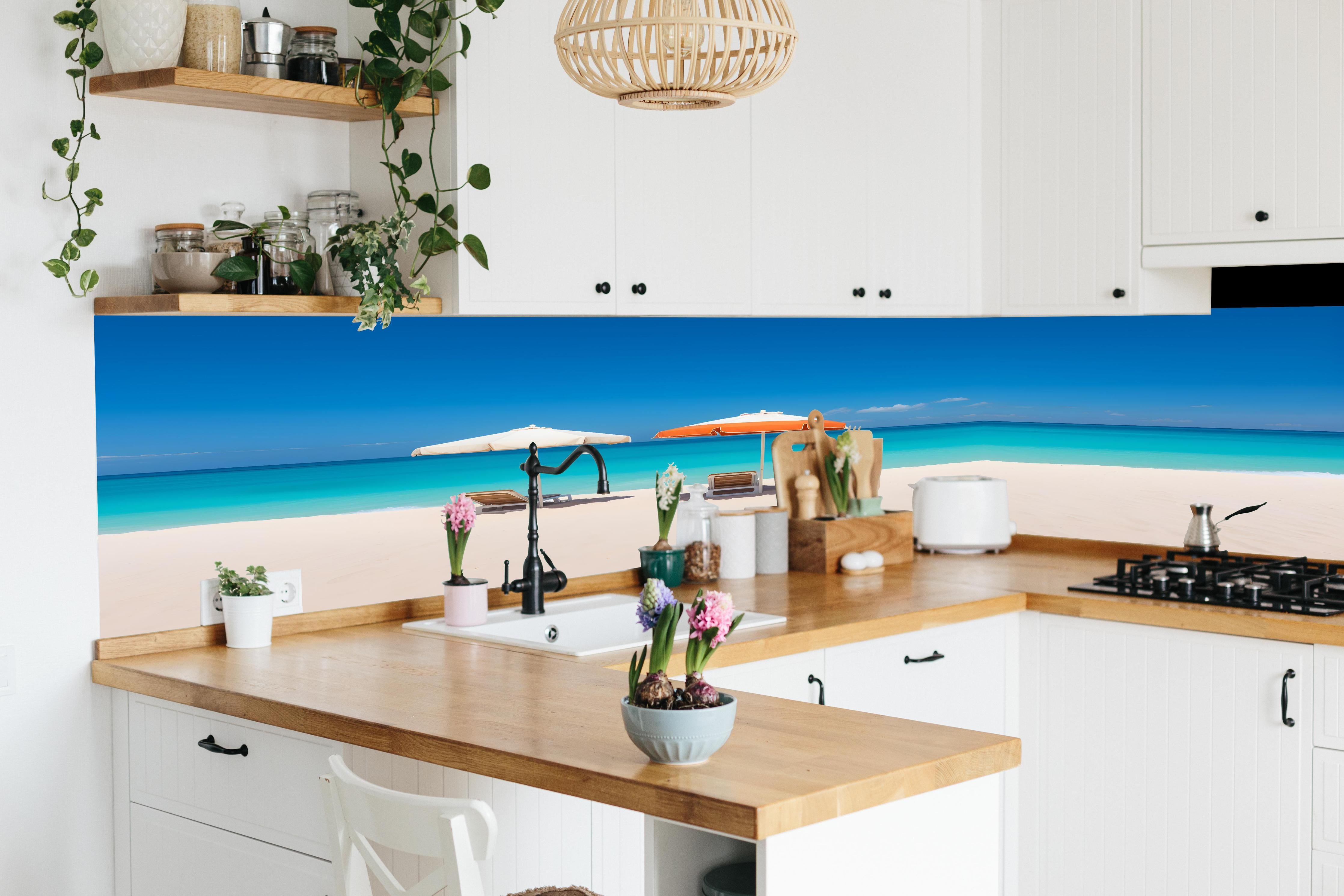 Küche - Idyllischer tropischer Strand mit weißen Sand und sonnigen Schirmen hinter weißen Hochglanz-Küchenregalen und schwarzem Wasserhahn