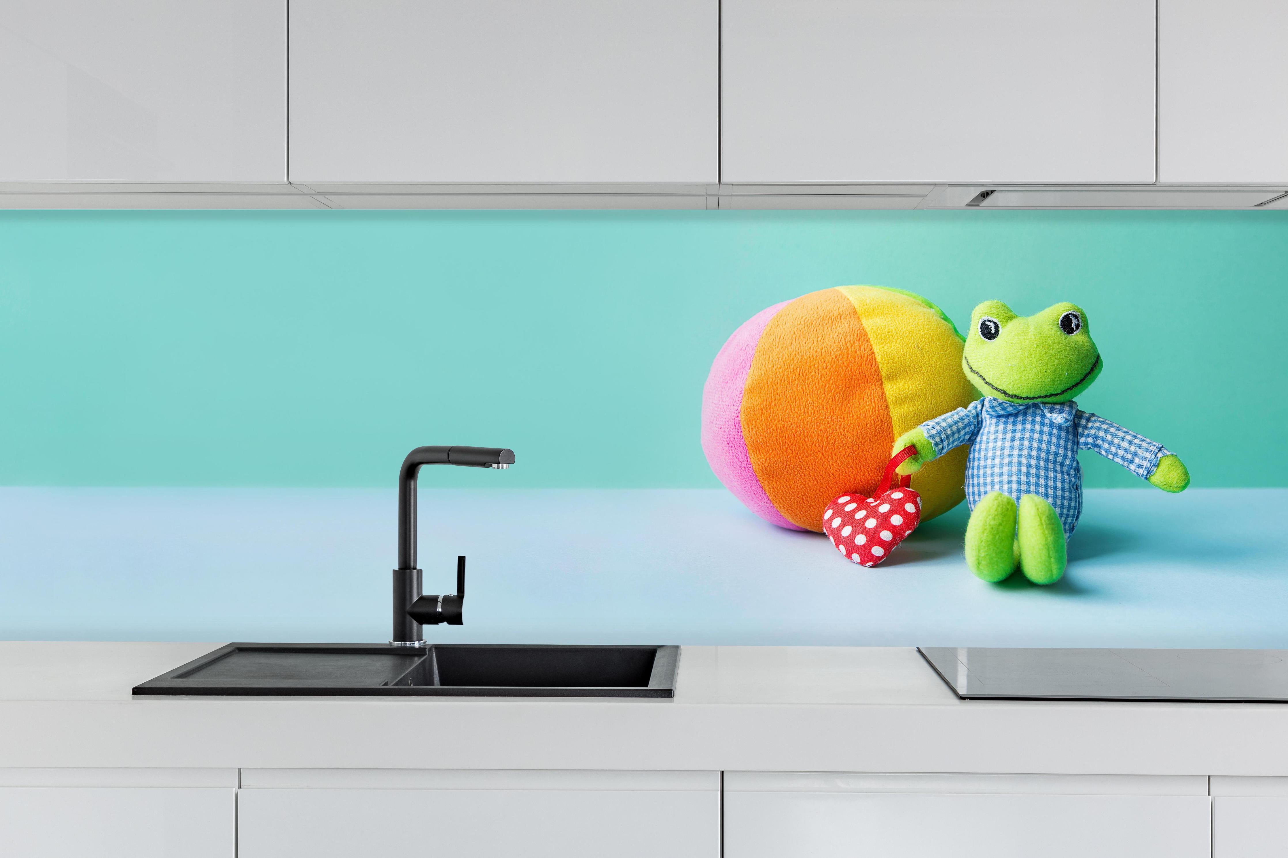 Küche - Kinderspielzeug Kleiner Frosch hinter weißen Hochglanz-Küchenregalen und schwarzem Wasserhahn