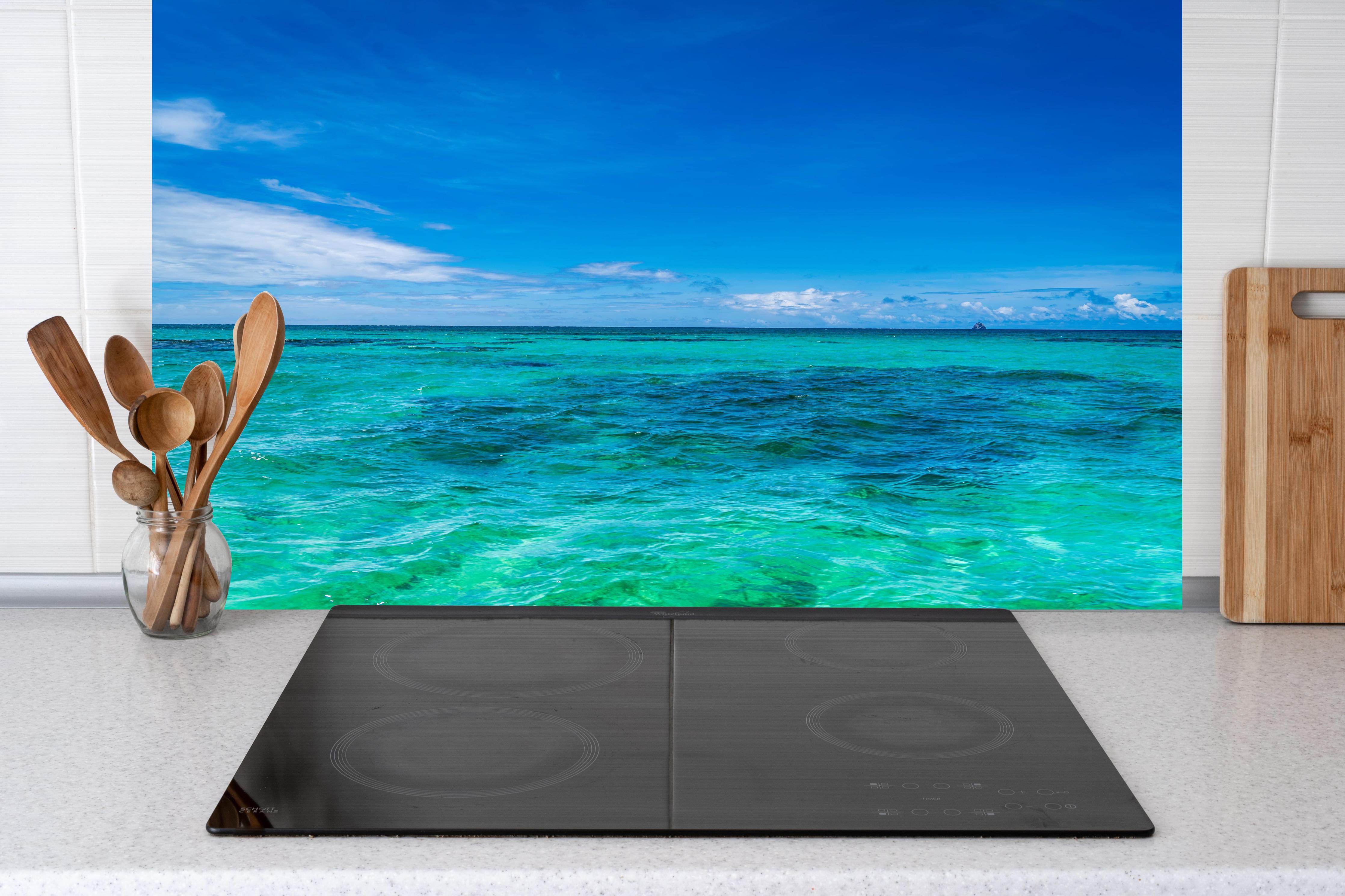 Küche - Klarmarkiertes, türkisblaues Wasser unter hellem Himmel hinter weißen Hochglanz-Küchenregalen und schwarzem Wasserhahn