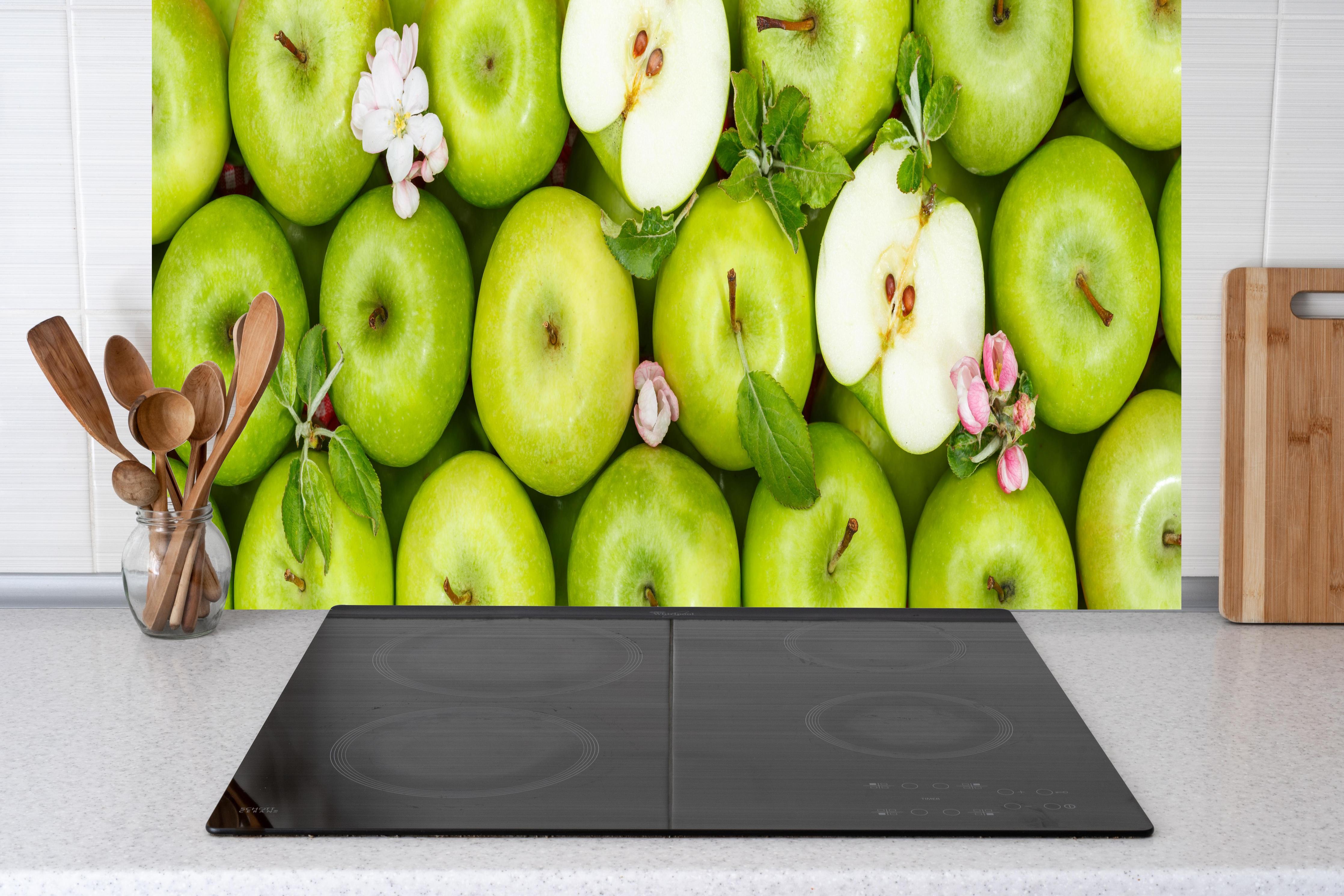 Küche - Frische grüne Äpfel hinter Cerankochfeld und Holz-Kochutensilien