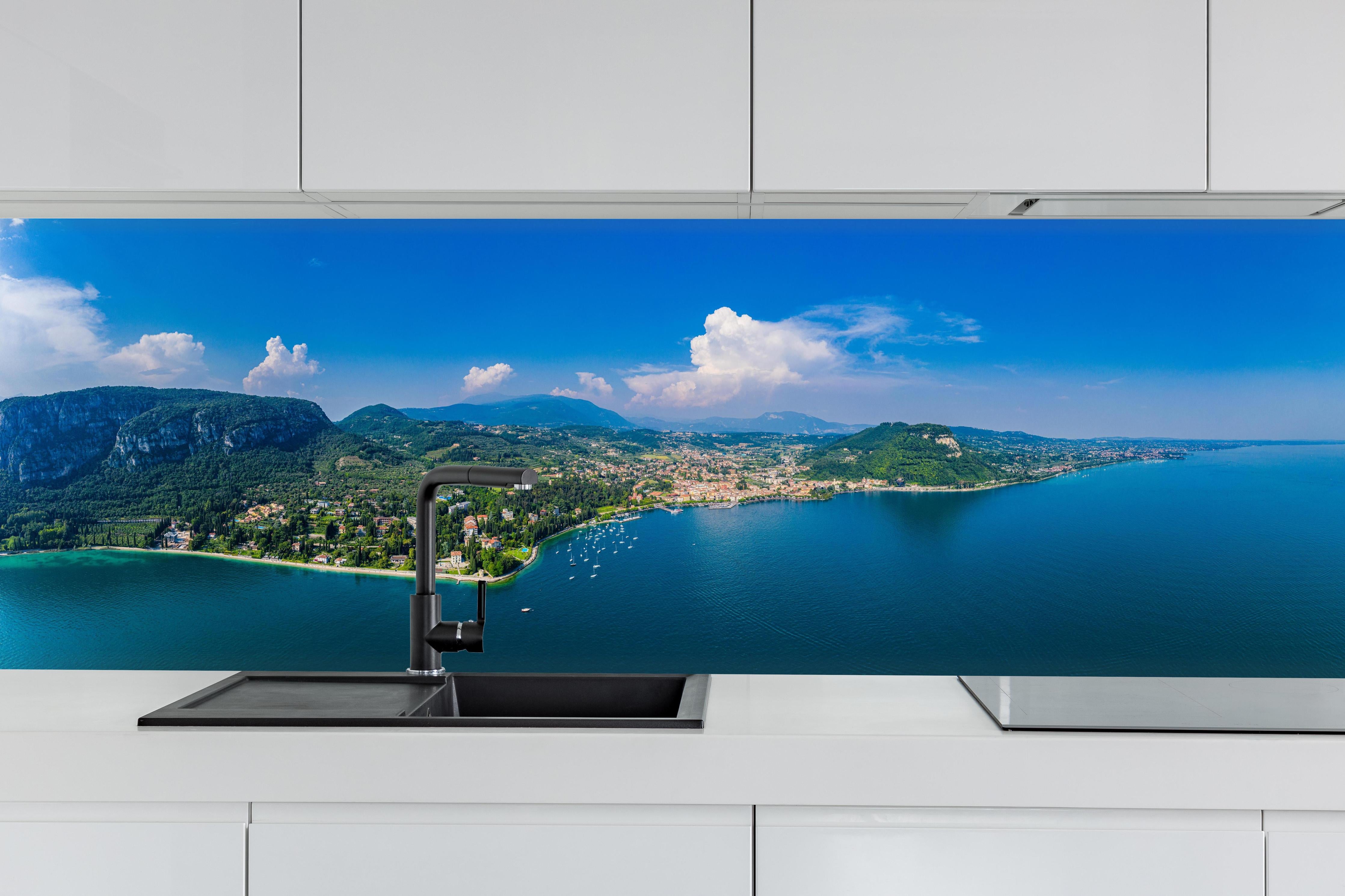 Küche - Gardasee Panorama Blau-Grün hinter weißen Hochglanz-Küchenregalen und schwarzem Wasserhahn