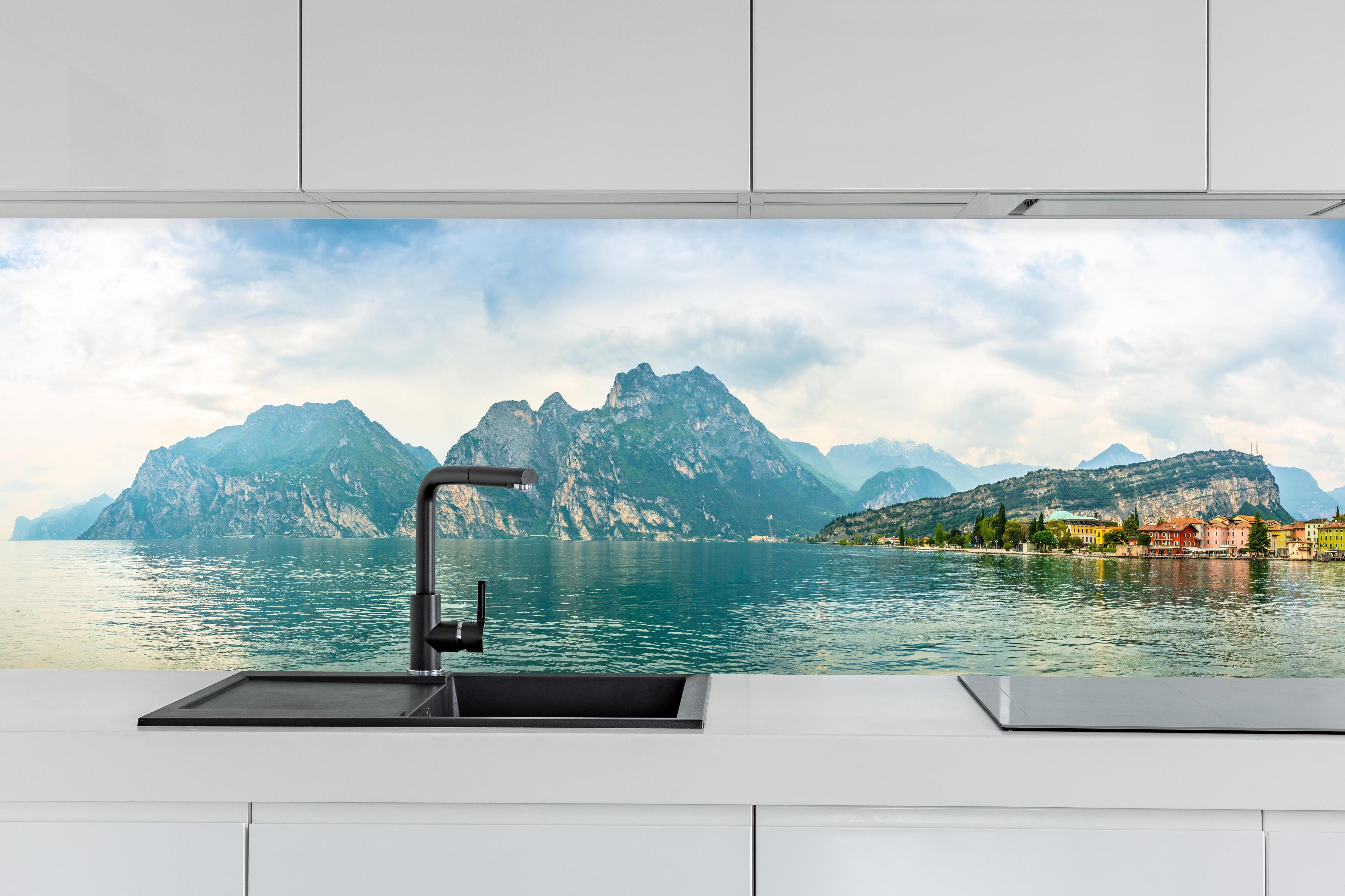 Küche - Gardasee im Farbenspiel von Himmel und Natur hinter weißen Hochglanz-Küchenregalen und schwarzem Wasserhahn