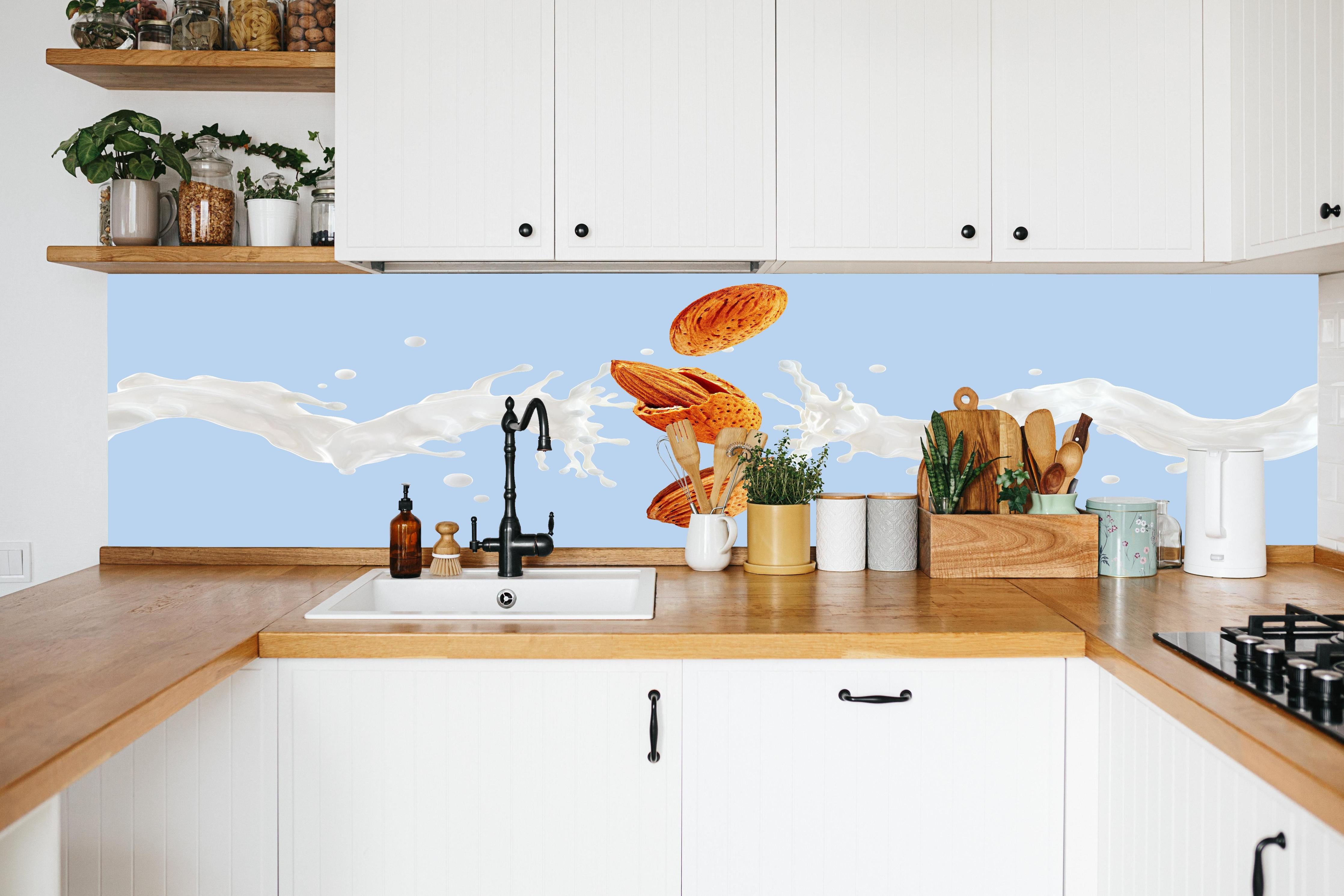 Küche - Mandelmilch-Splash auf Blau in weißer Küche hinter Gewürzen und Kochlöffeln aus Holz