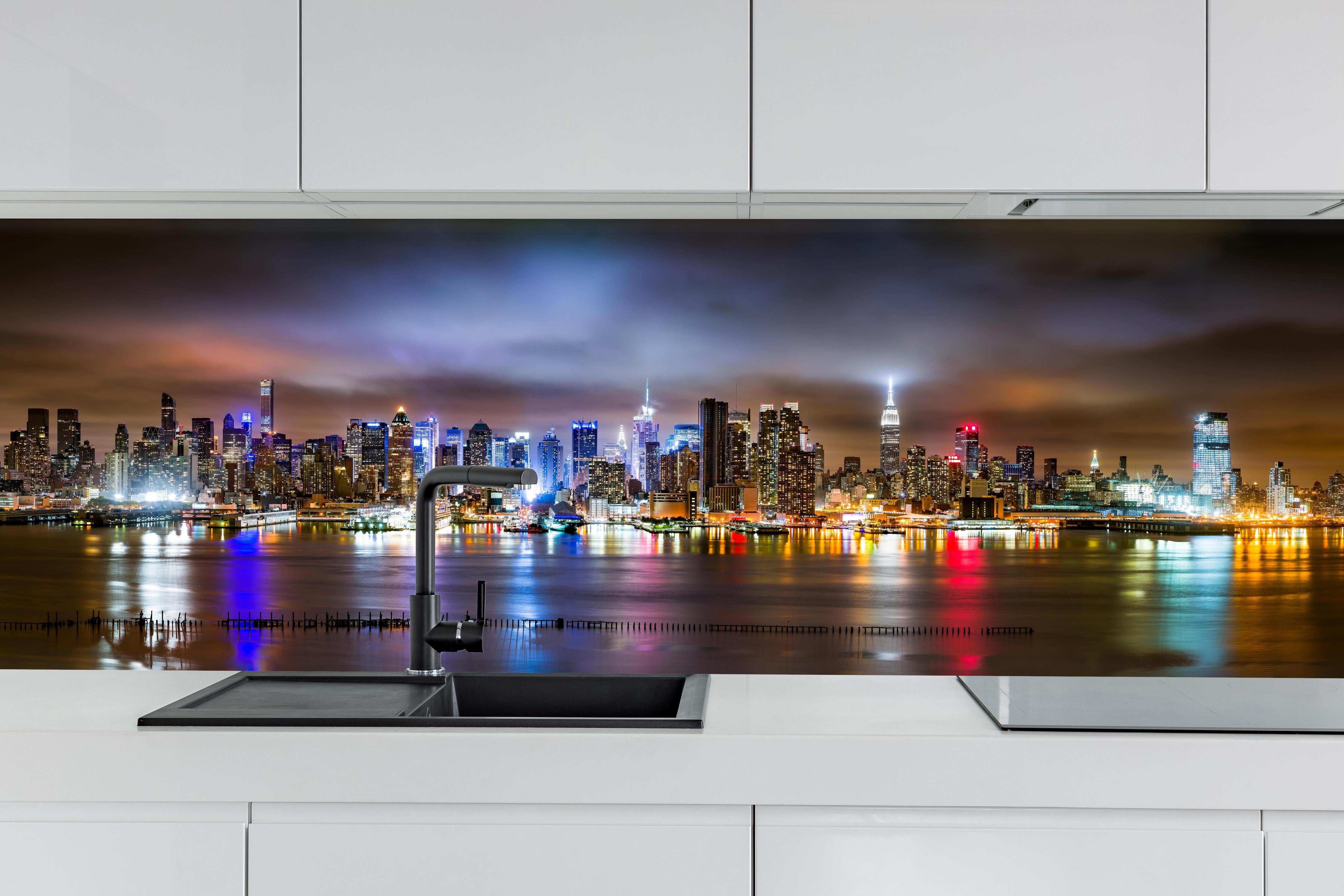 Küche - Manhattan Skyline im nächtlichen Panorama hinter weißen Hochglanz-Küchenregalen und schwarzem Wasserhahn