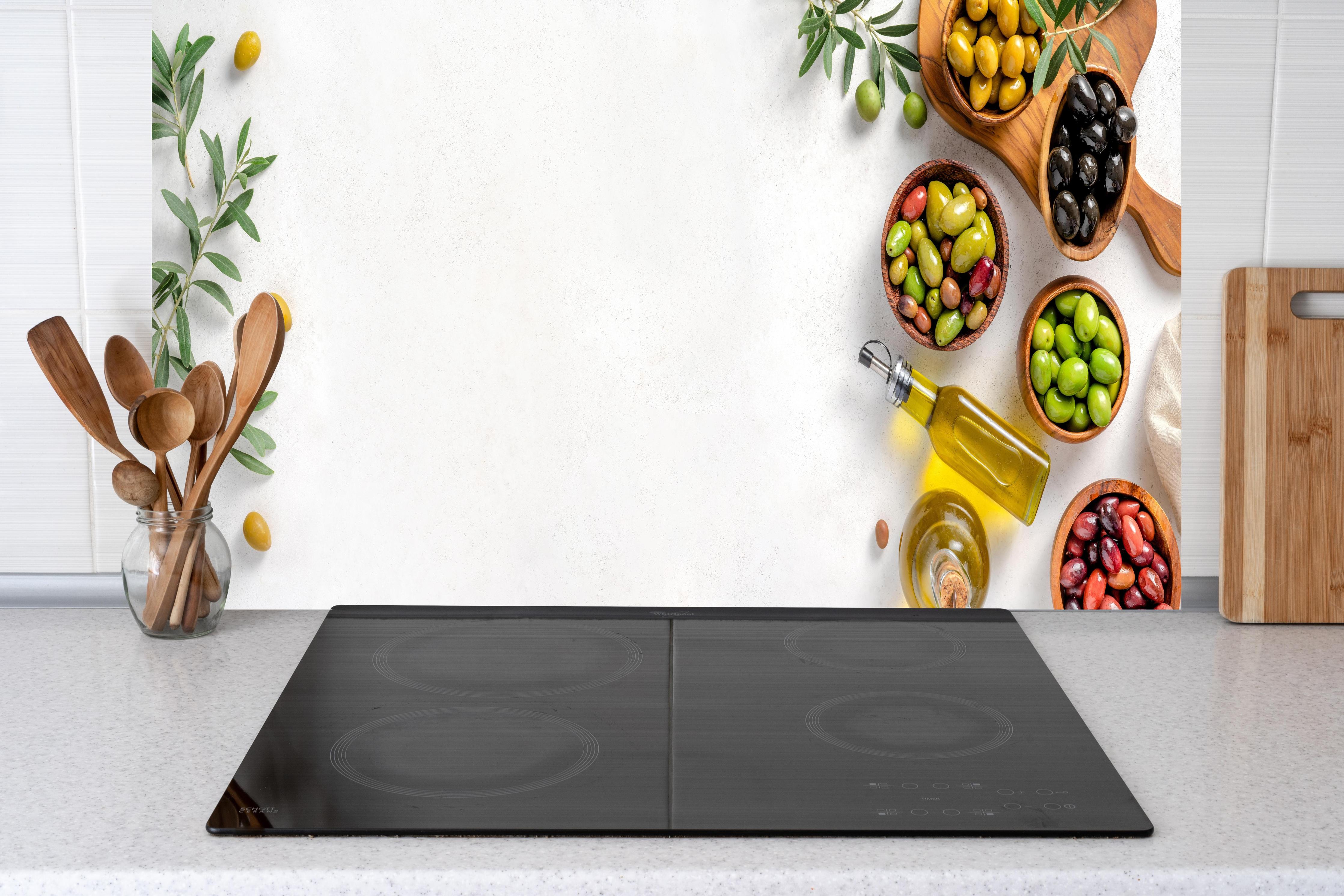 Küche - Mediterrane Oliven auf Weiß hinter Cerankochfeld und Holz-Kochutensilien
