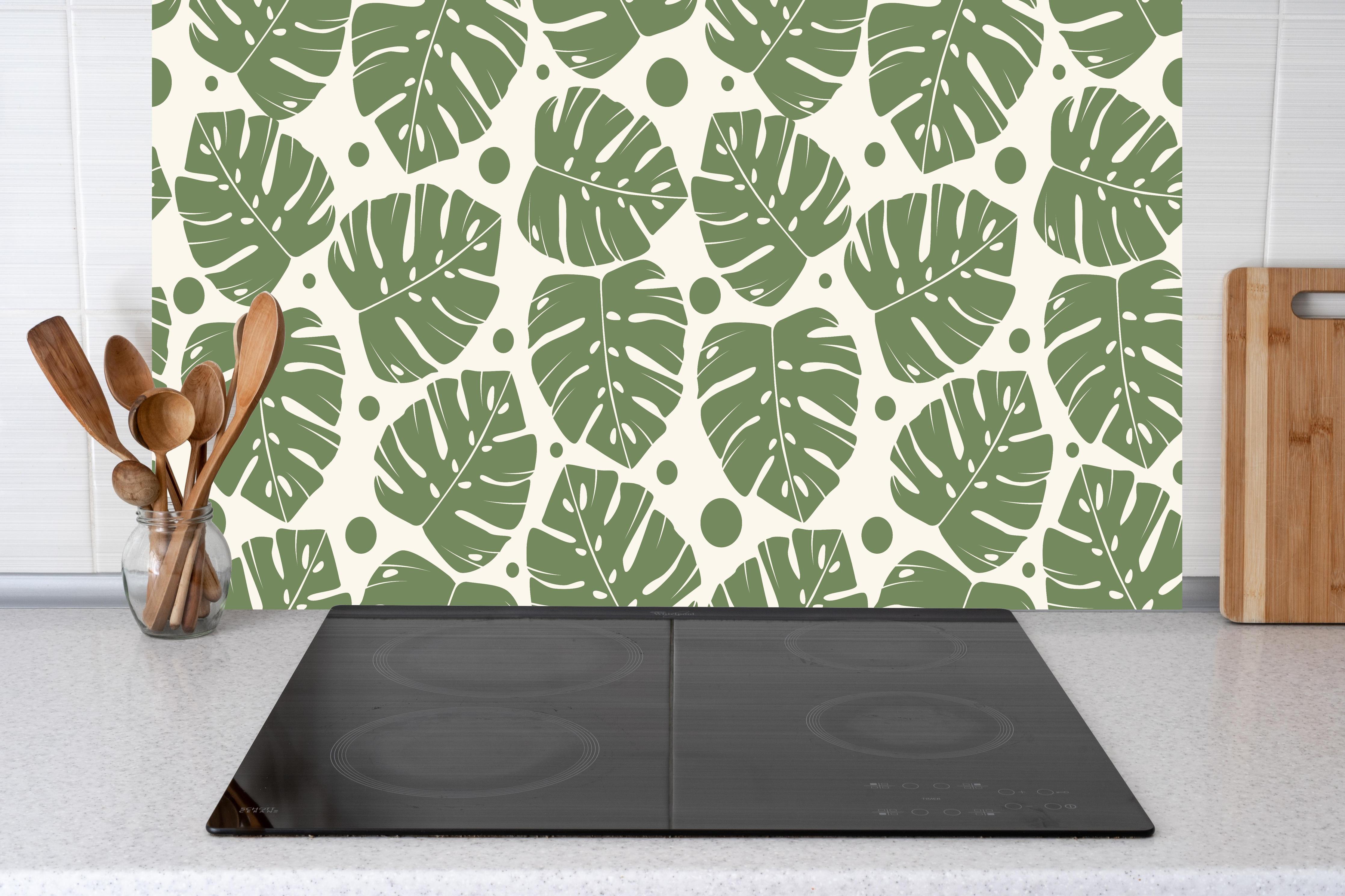 Küche - Monstera-Blätter Cremegrün hinter Cerankochfeld und Holz-Kochutensilien