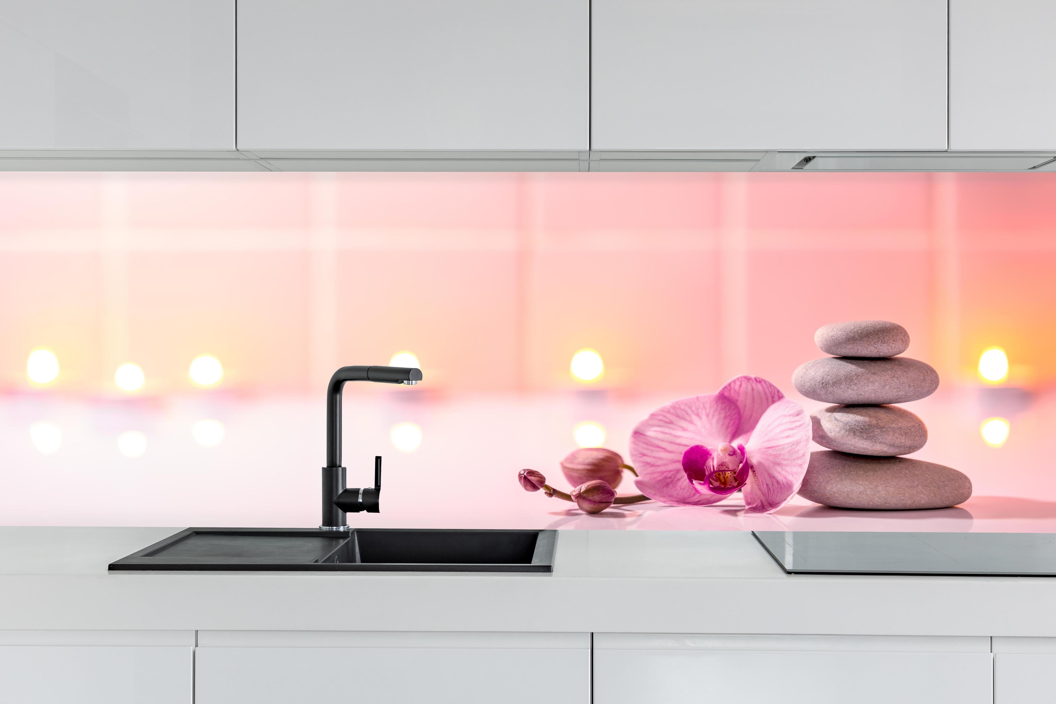 Küche - Rosa Orchidee mit Zen-Steinen hinter weißen Hochglanz-Küchenregalen und schwarzem Wasserhahn