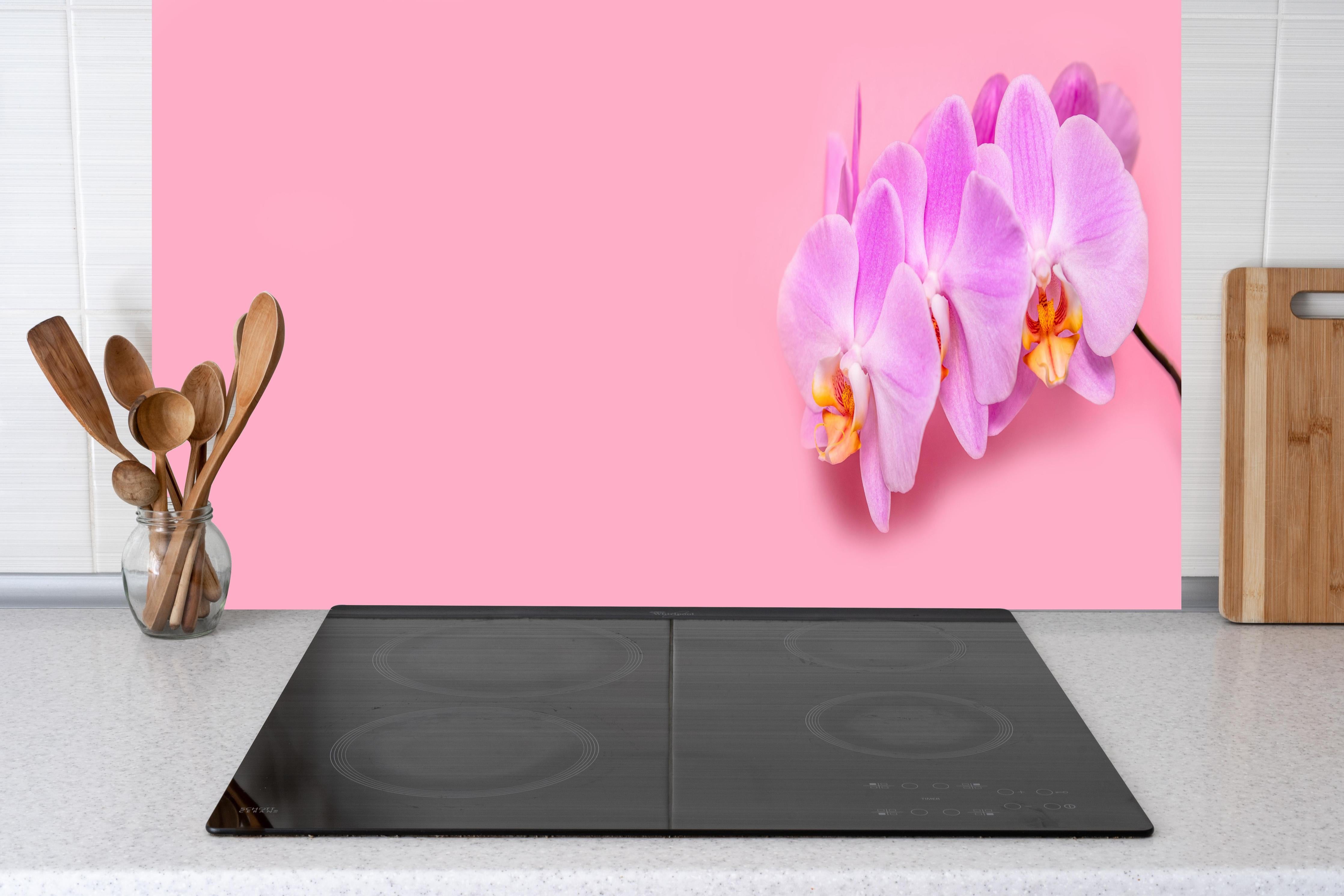 Küche - Rosa Orchideen auf Pink hinter Cerankochfeld und Holz-Kochutensilien