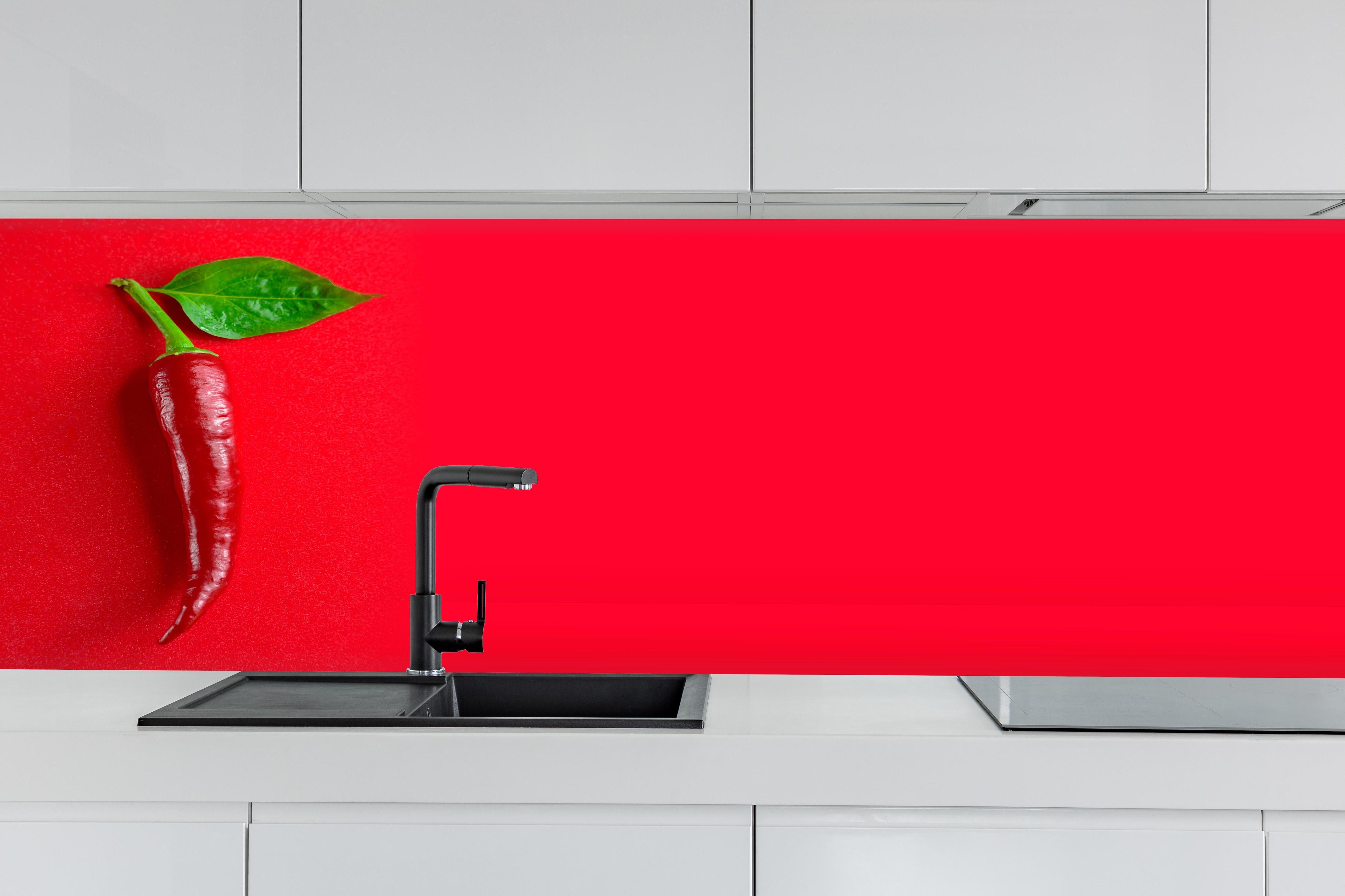 Küche - Rote Chili mit grünem Blatt hinter weißen Hochglanz-Küchenregalen und schwarzem Wasserhahn