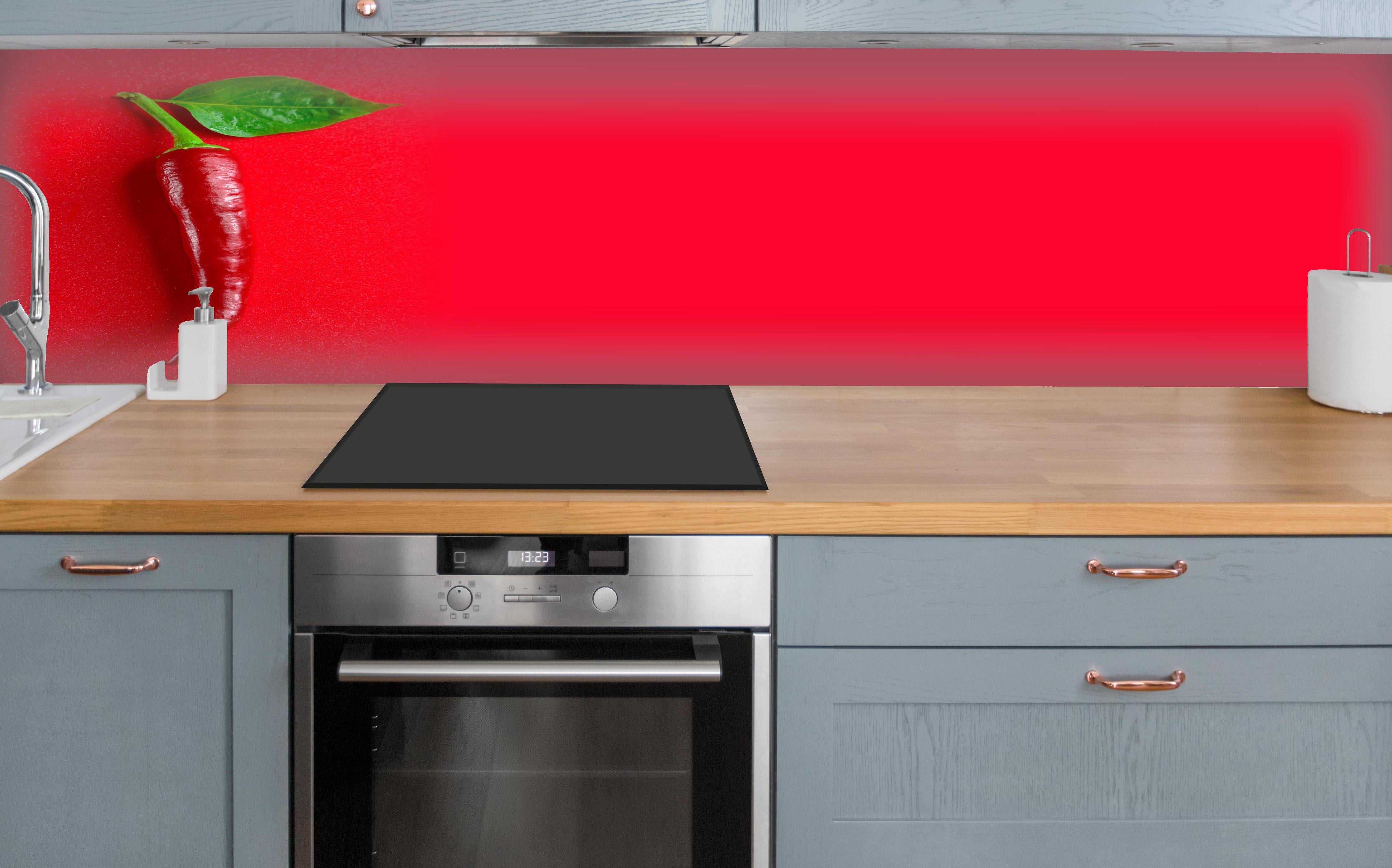 Küche - Rote Chili mit grünem Blatt über polierter Holzarbeitsplatte mit Cerankochfeld