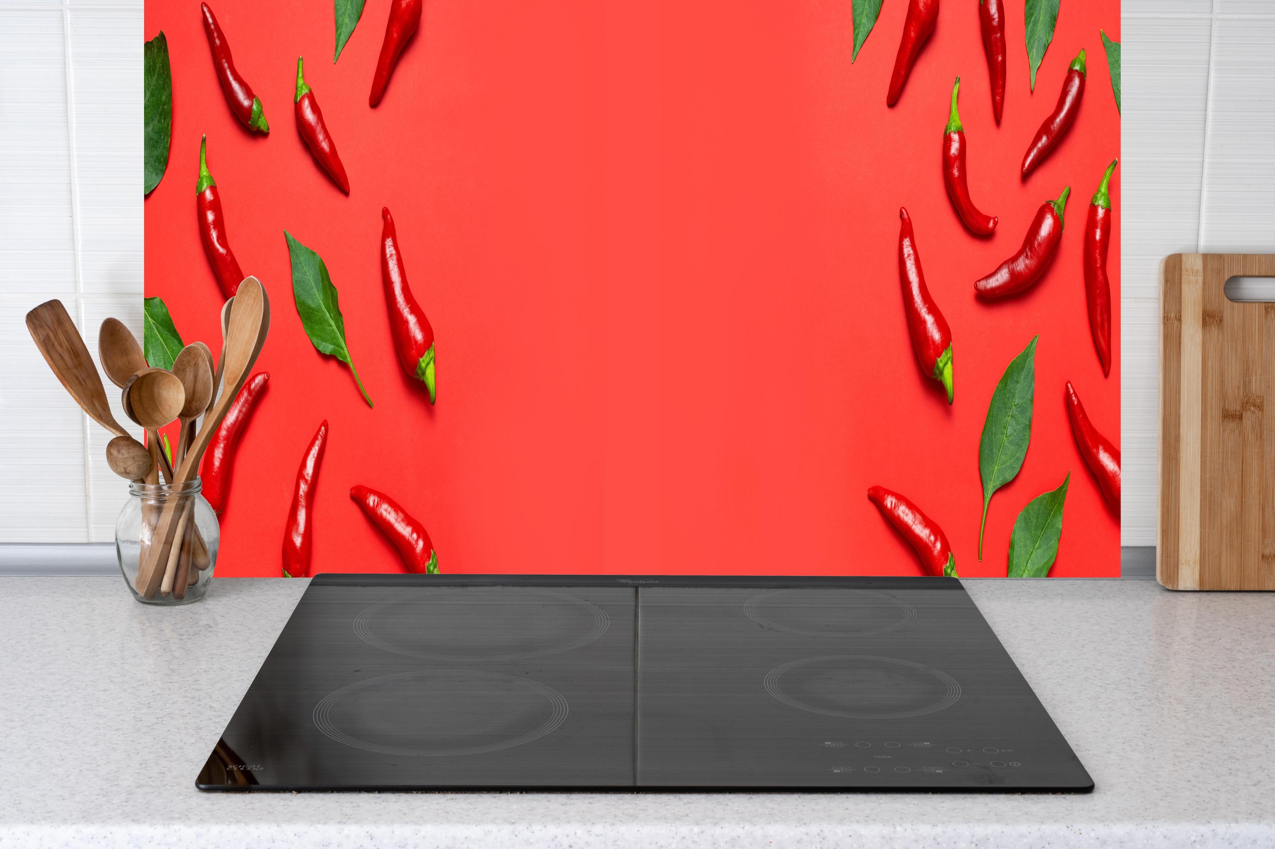 Küche - Rote Chili mit grünen Blättern hinter Cerankochfeld und Holz-Kochutensilien