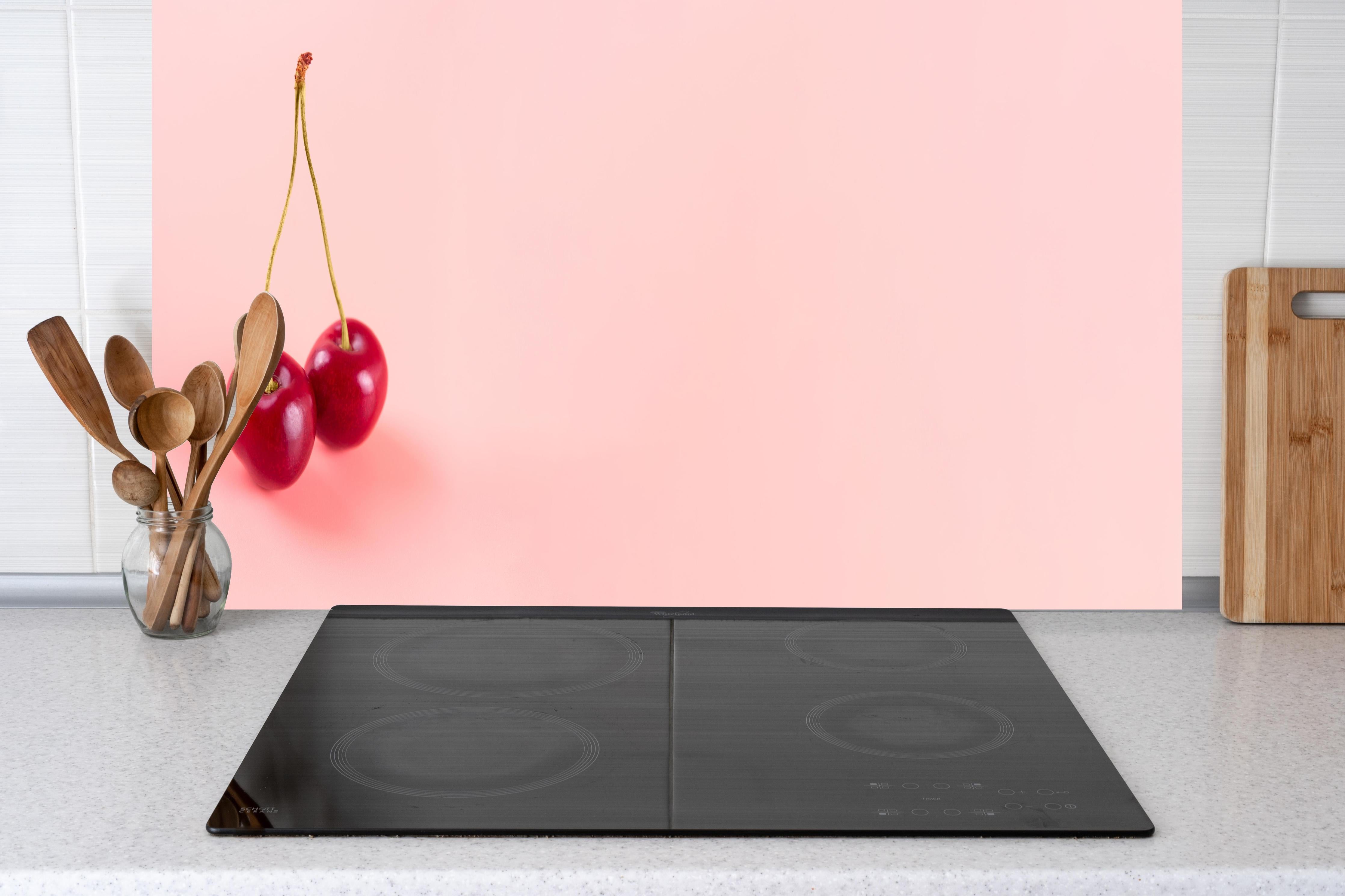 Küche - Rote Kirschen auf Rosa Hintergrund hinter Cerankochfeld und Holz-Kochutensilien