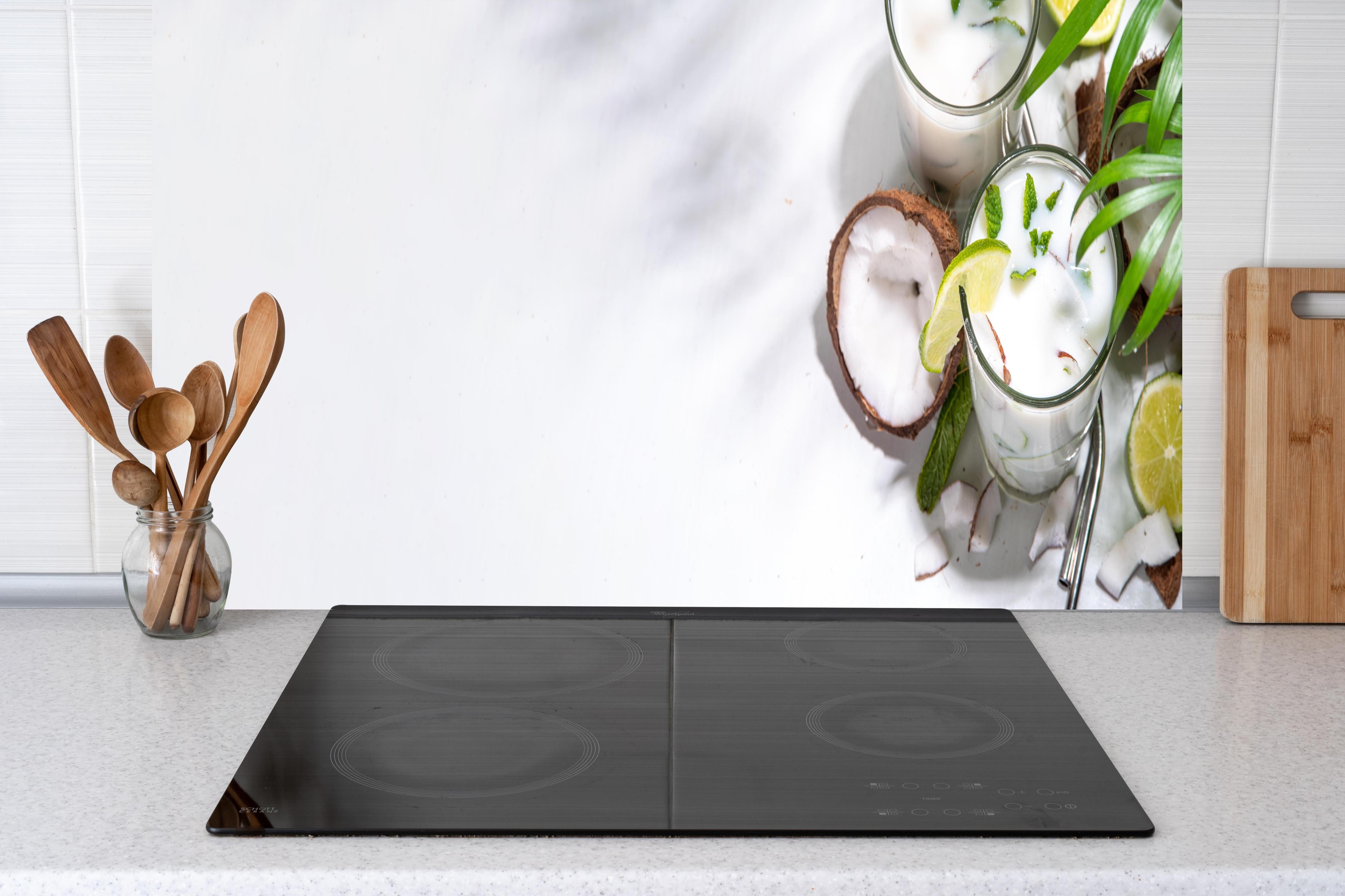 Küche - Weißer Kokosdrink mit Limette hinter Cerankochfeld und Holz-Kochutensilien