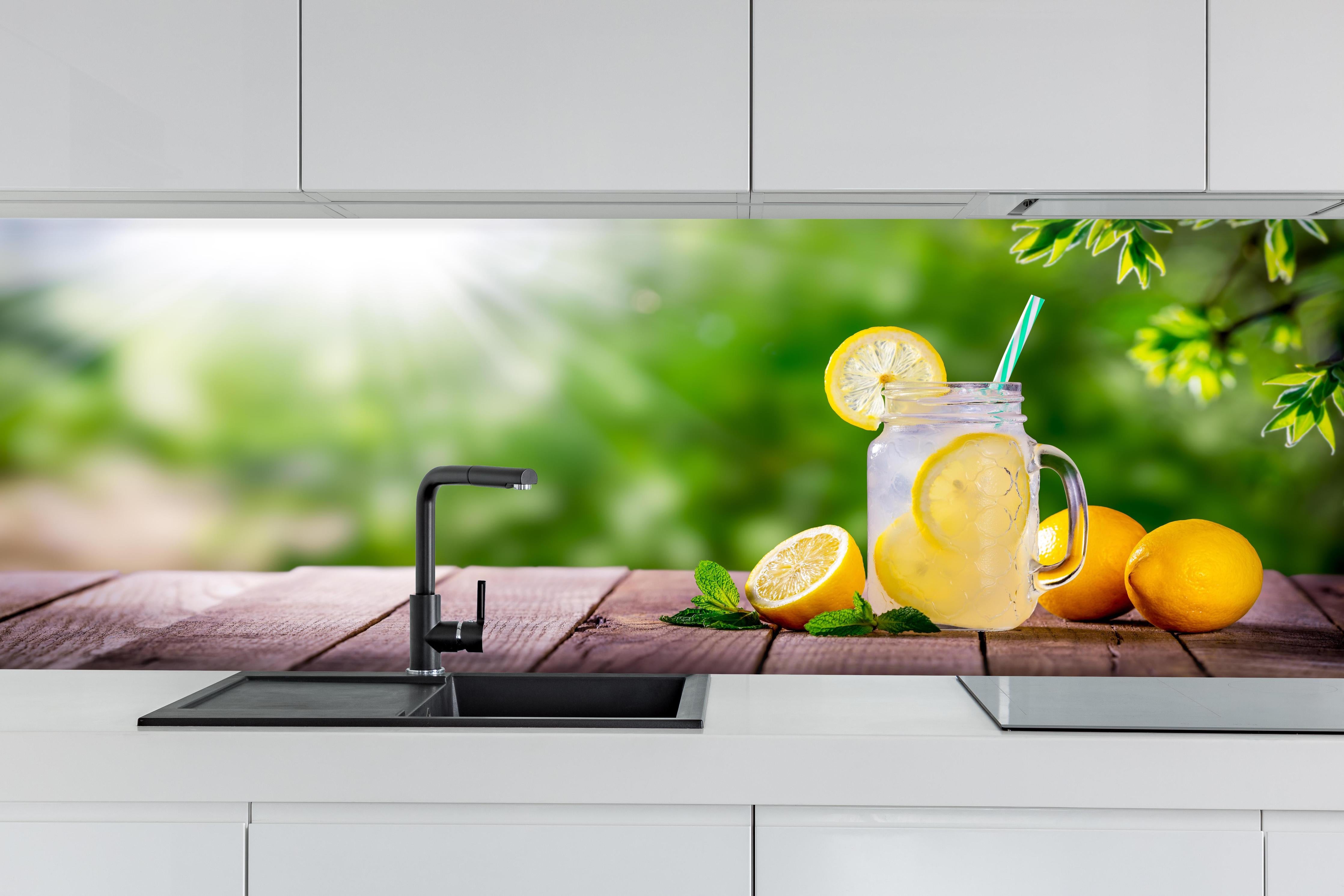 Küche - Zitronen-Limonade auf Holztisch hinter weißen Hochglanz-Küchenregalen und schwarzem Wasserhahn