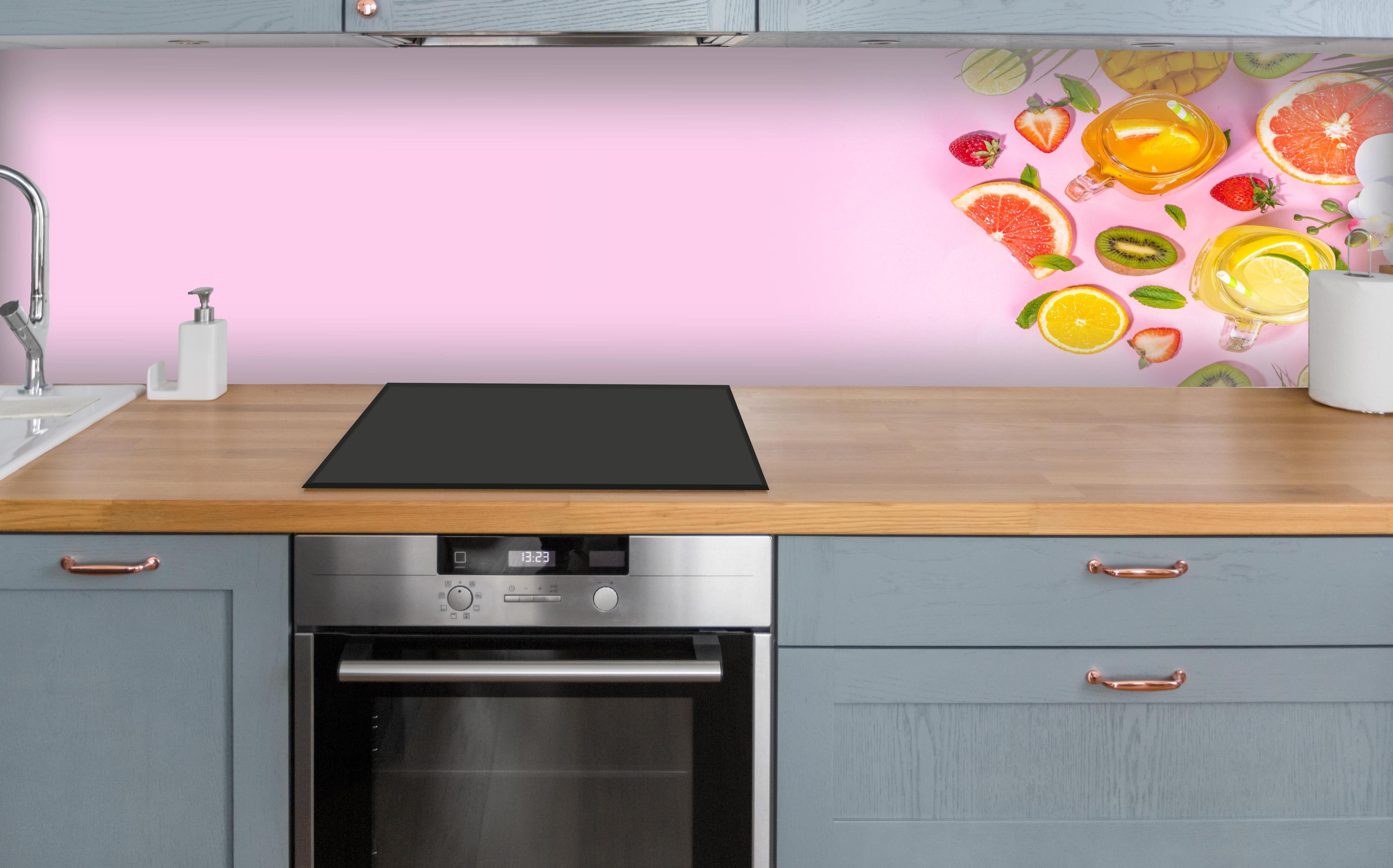 Küche - Zitrusfrüchte auf rosa Hintergrund über polierter Holzarbeitsplatte mit Cerankochfeld