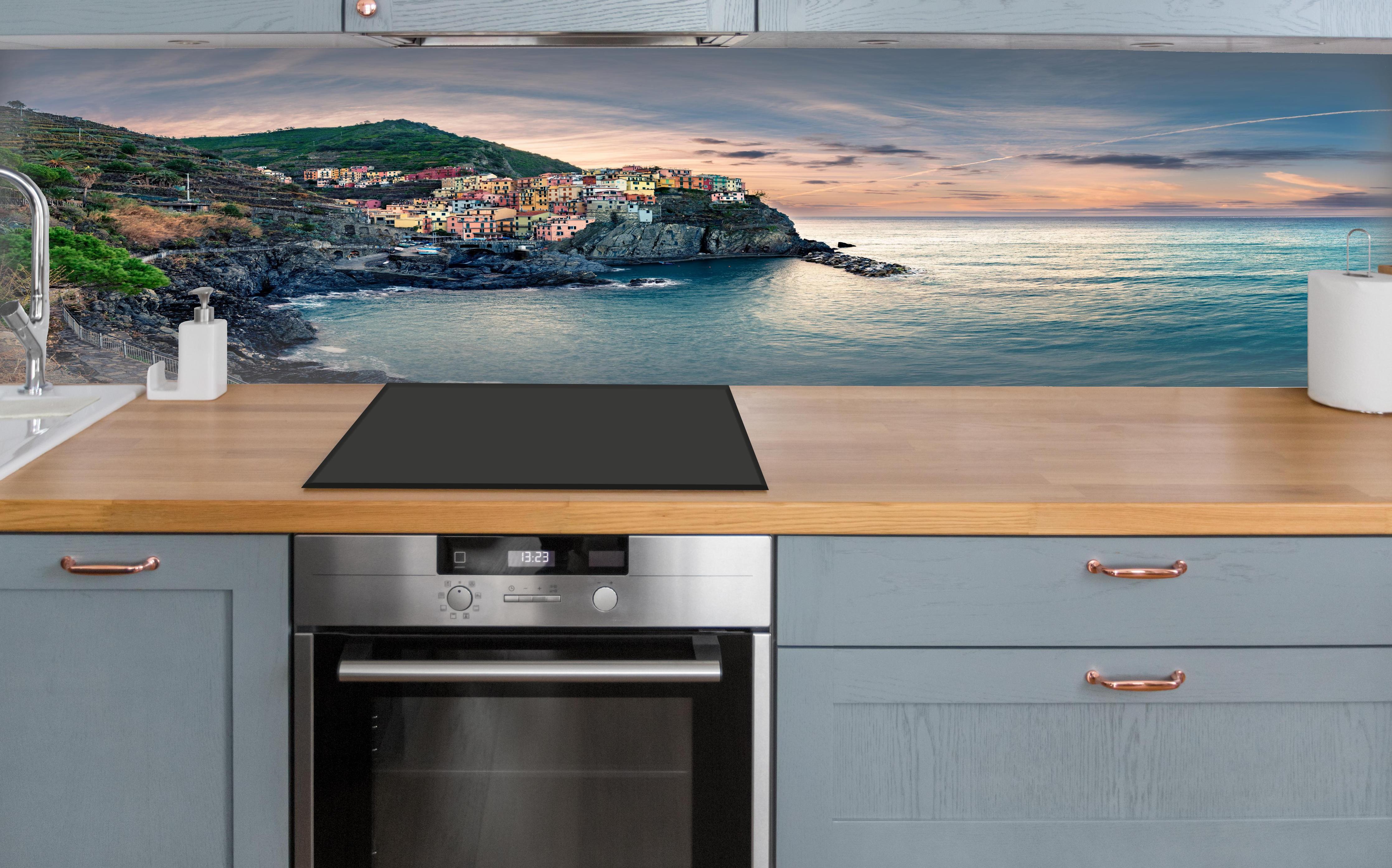 Küche - talienische Küste im Abendrot über polierter Holzarbeitsplatte mit Cerankochfeld