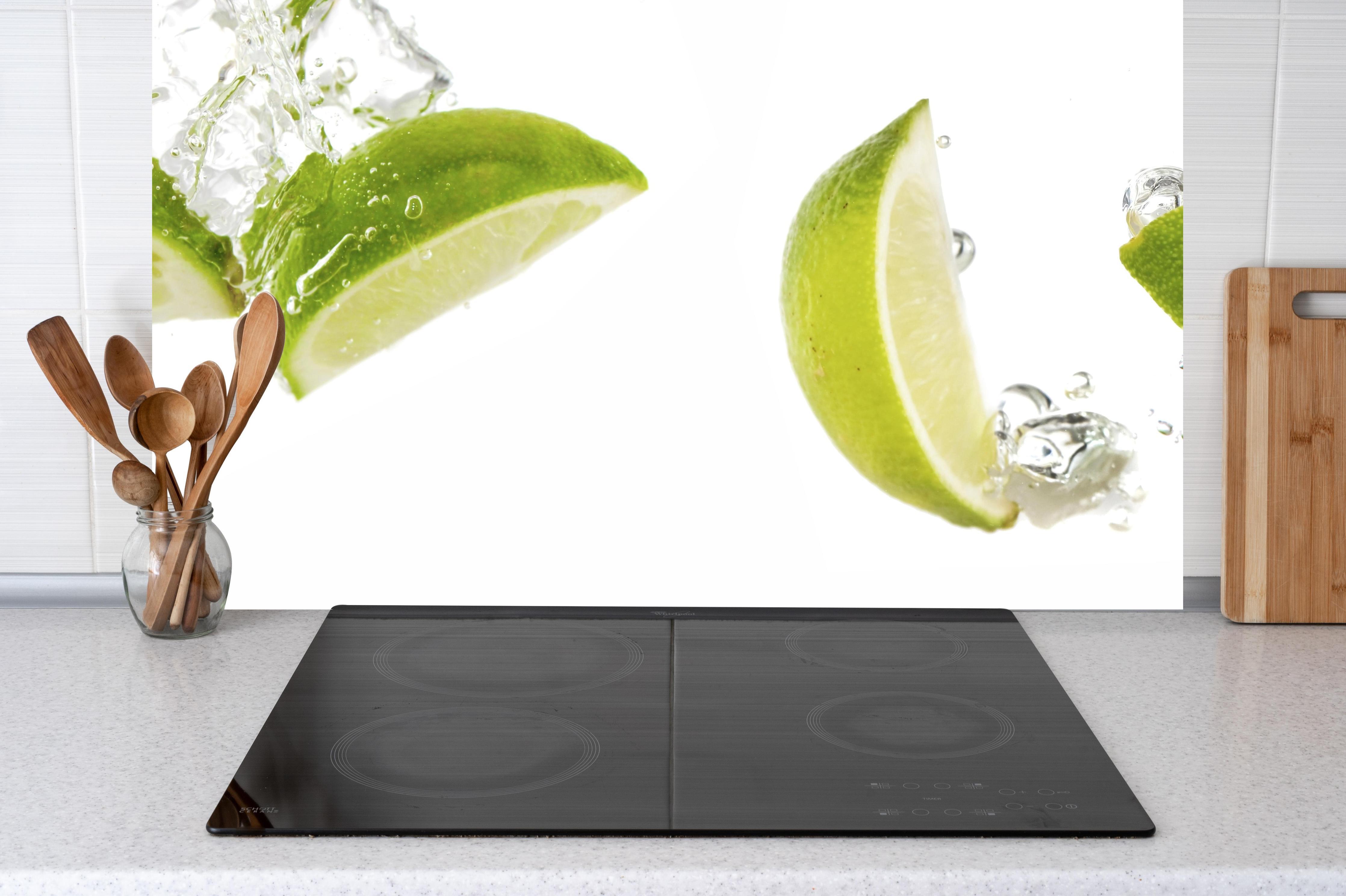 Küche - Frische Limette in Wasser hinter Cerankochfeld und Holz-Kochutensilien