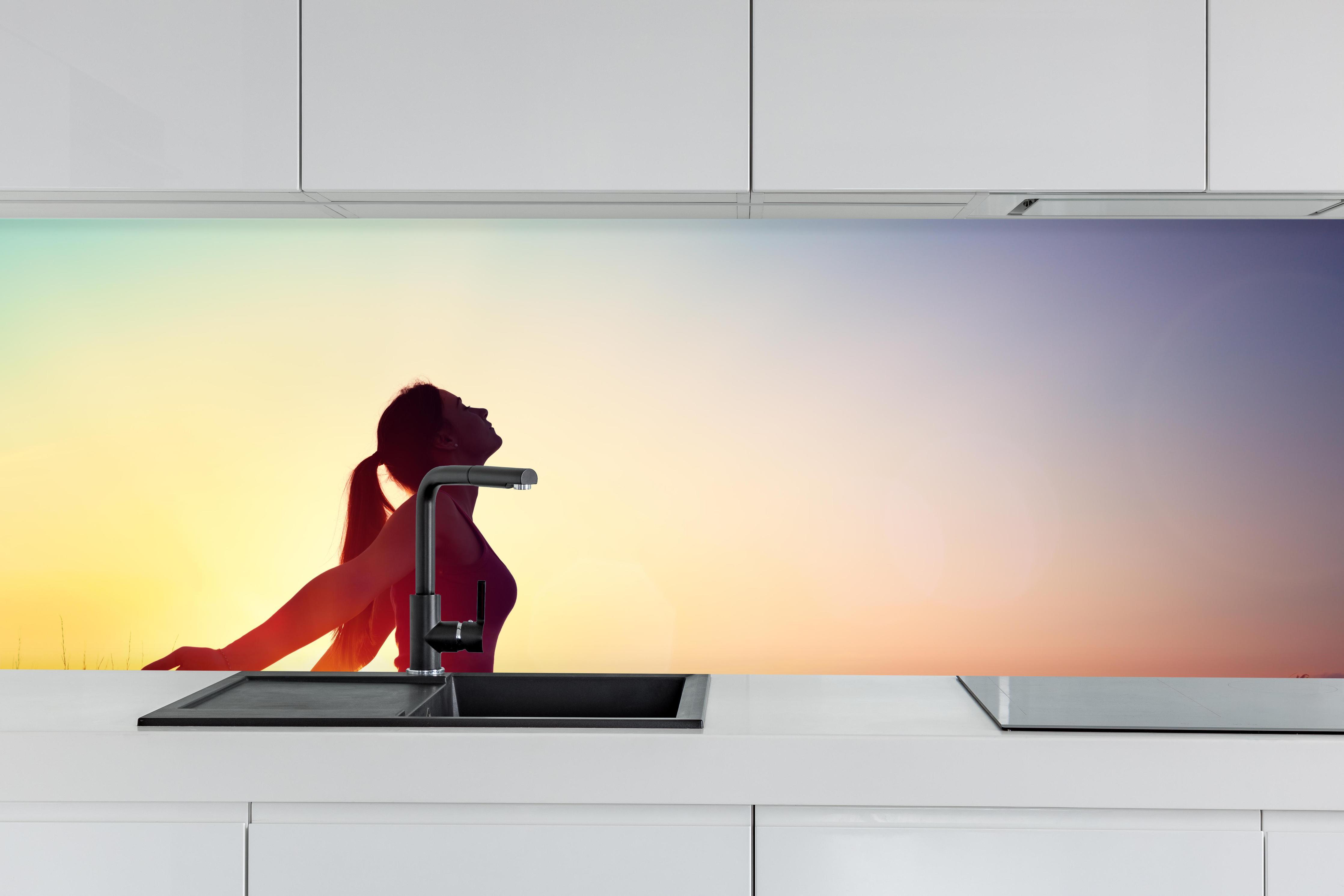 Küche - Glückliche Frau beim Sonnenuntergang hinter weißen Hochglanz-Küchenregalen und schwarzem Wasserhahn