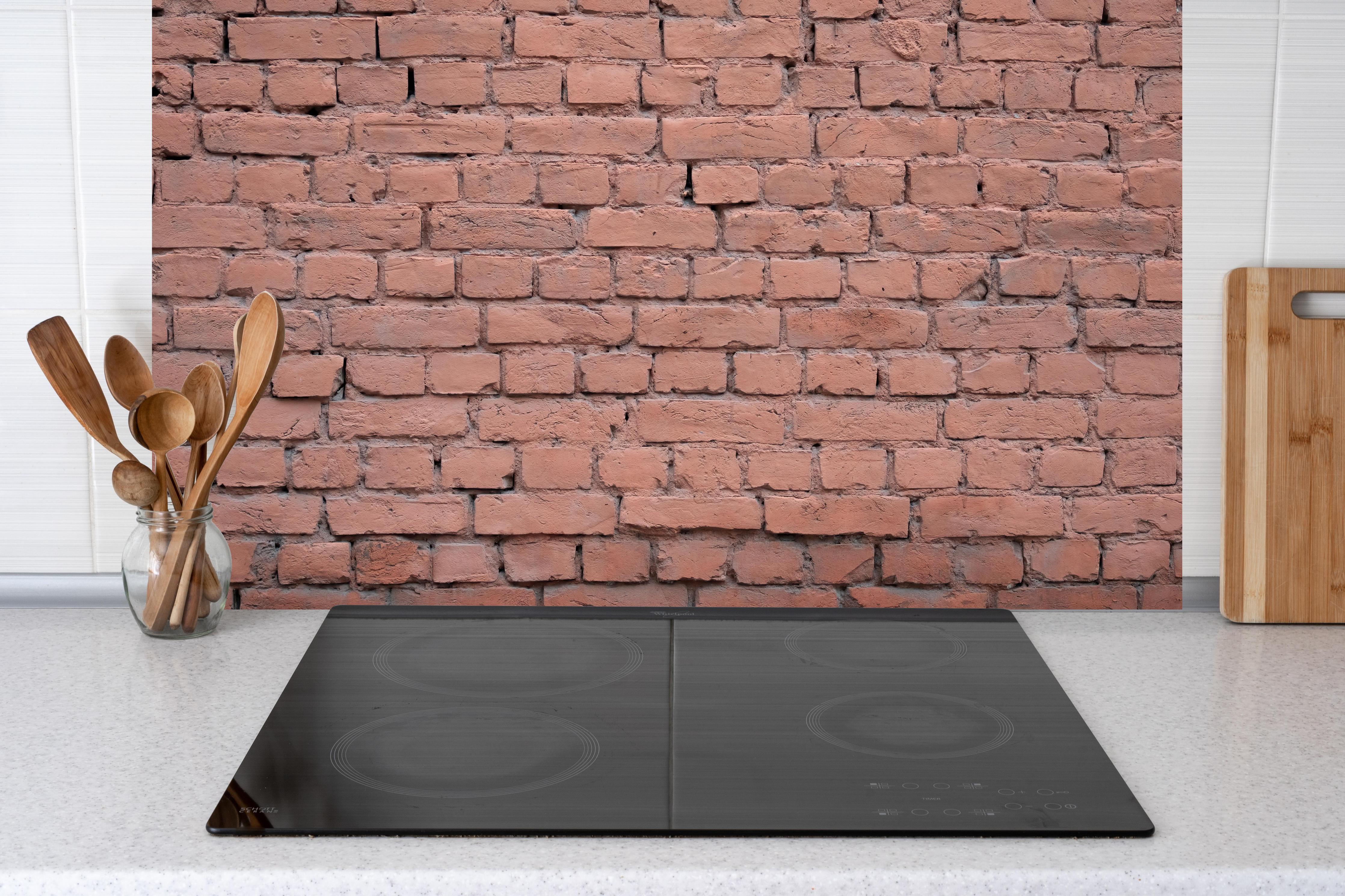 Küche - Rosafarbige Ziegelwandoberfläche hinter Cerankochfeld und Holz-Kochutensilien