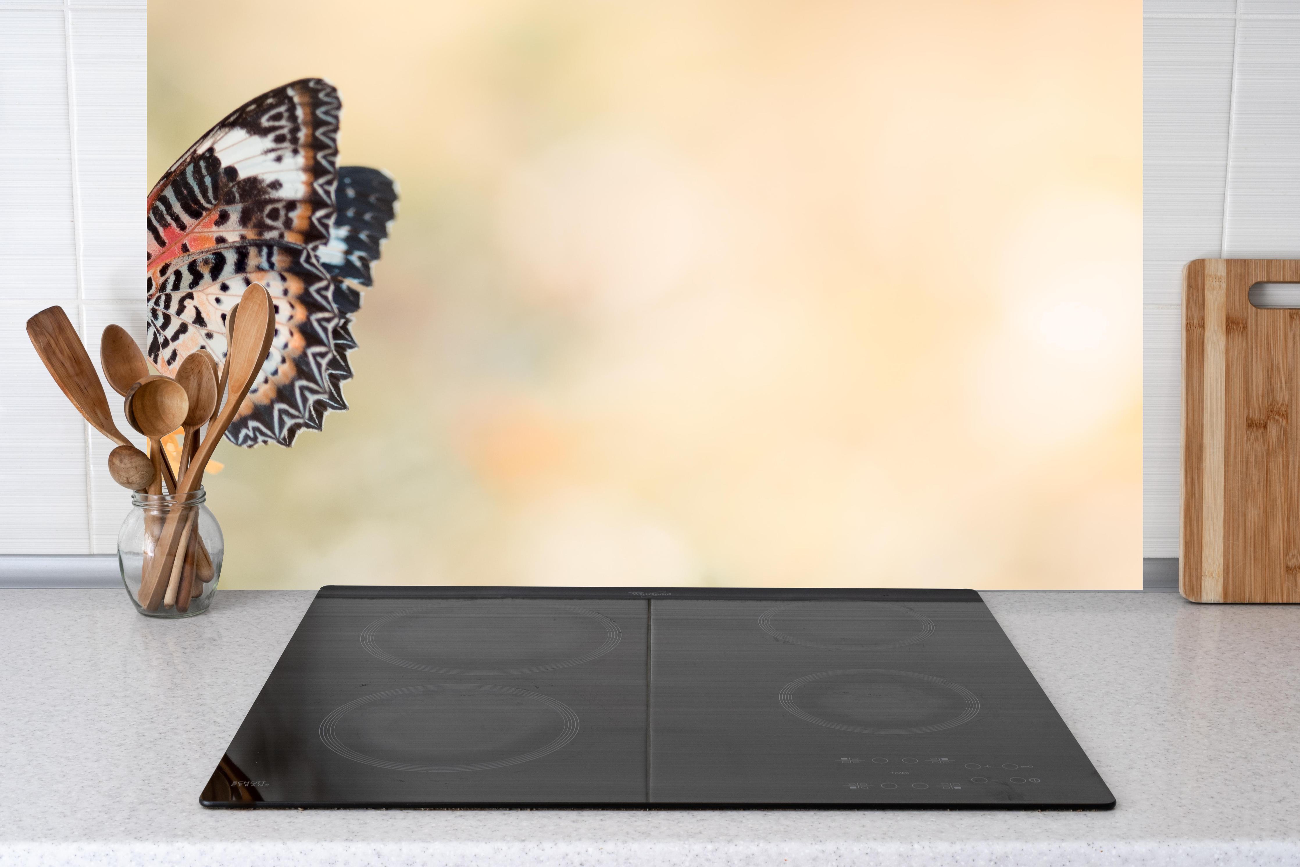 Küche - Schmetterling auf eine orangene Blume hinter Cerankochfeld und Holz-Kochutensilien