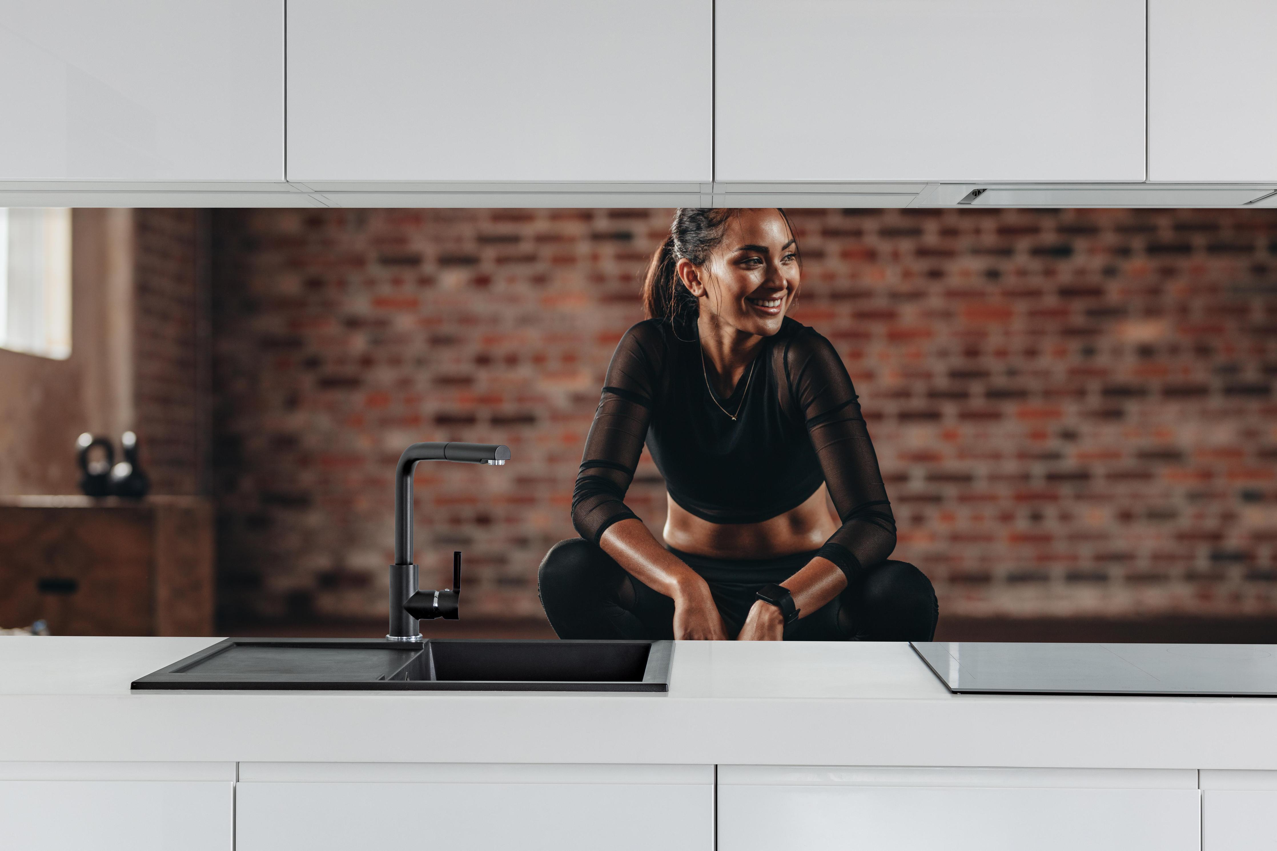 Küche - Sportlerin in der Hocke hinter weißen Hochglanz-Küchenregalen und schwarzem Wasserhahn