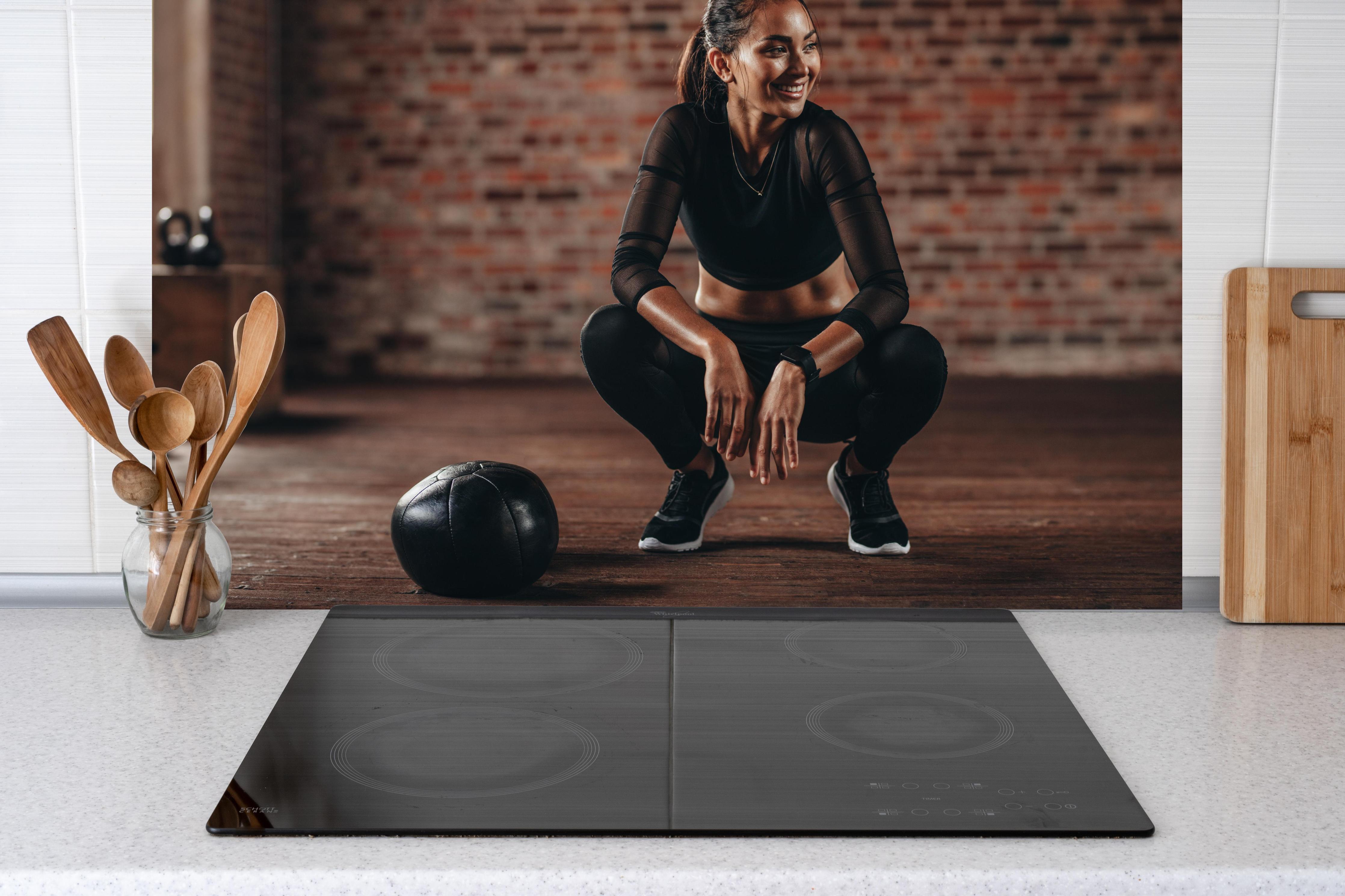 Küche - Sportlerin in der Hocke hinter Cerankochfeld und Holz-Kochutensilien