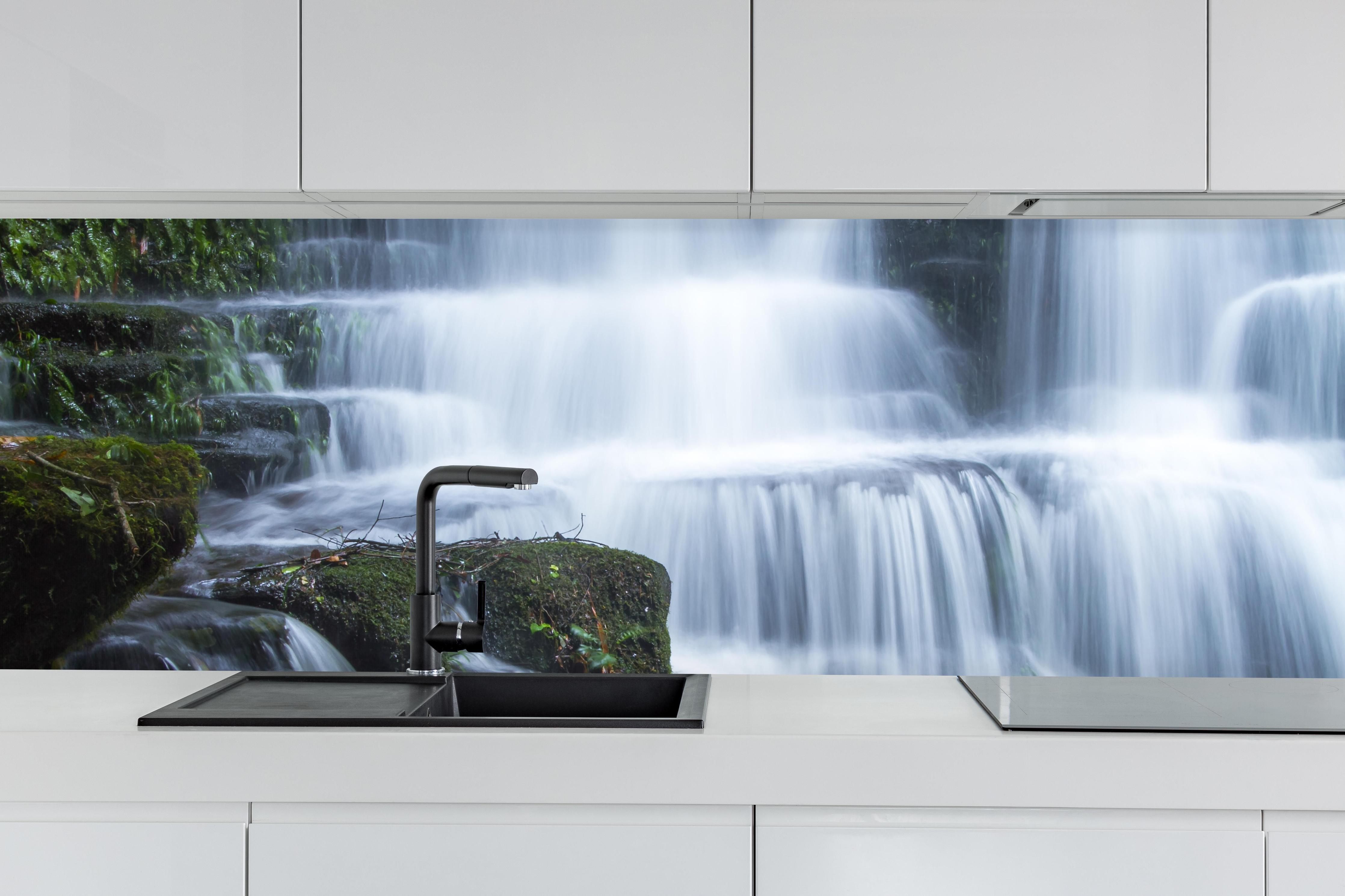 Küche - Wasserfall im Wald mit Felsen hinter weißen Hochglanz-Küchenregalen und schwarzem Wasserhahn
