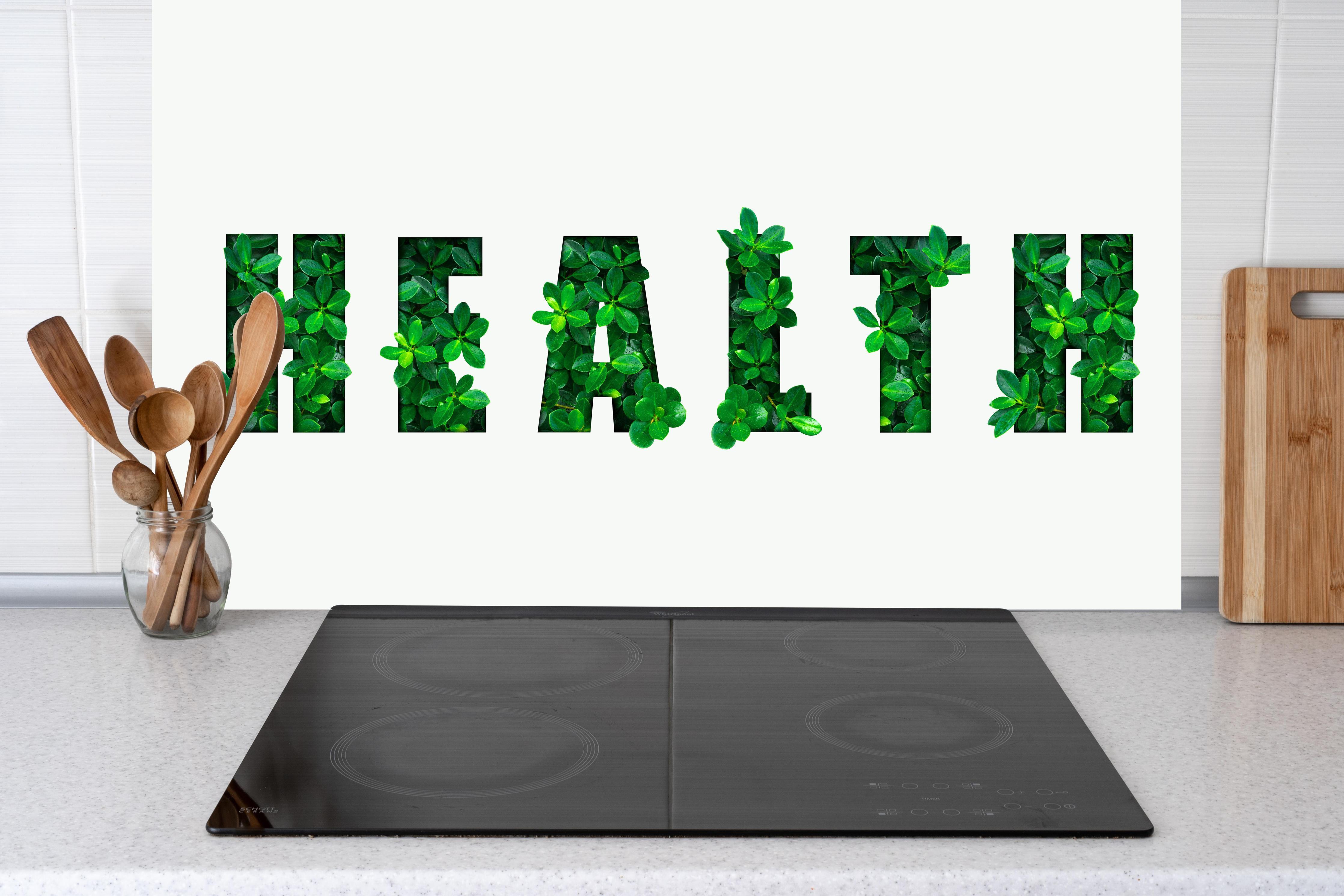 Küche - Wort HEALTH aus grünen Blättern hinter Cerankochfeld und Holz-Kochutensilien