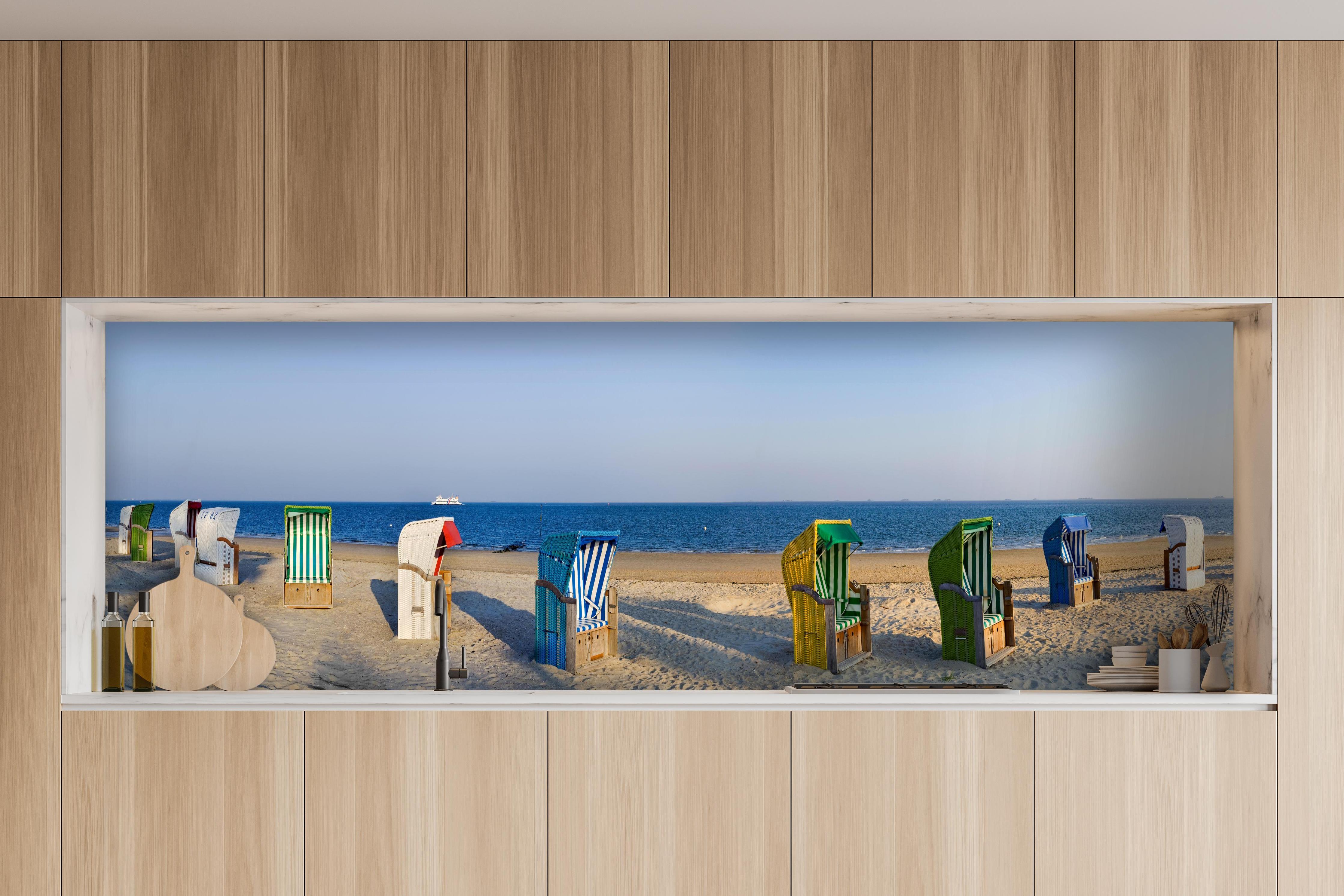 Küche - Kunstvolle, bunte Strandkörbe am Sandstrand mit Blick aufs Meer hinter weißen Hochglanz-Küchenregalen und schwarzem Wasserhahn