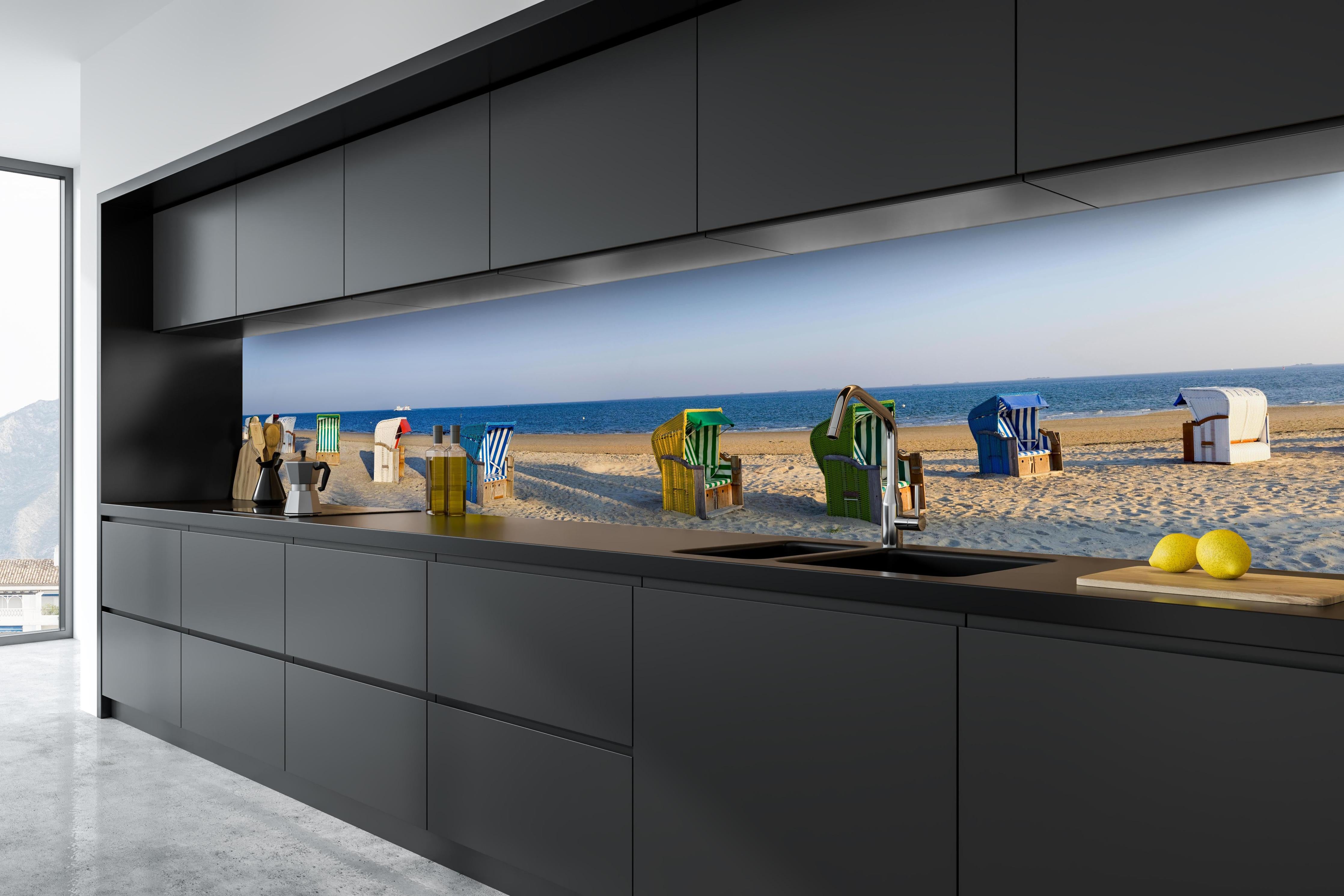 Küche - Kunstvolle, bunte Strandkörbe am Sandstrand mit Blick aufs Meer hinter weißen Hochglanz-Küchenregalen und schwarzem Wasserhahn