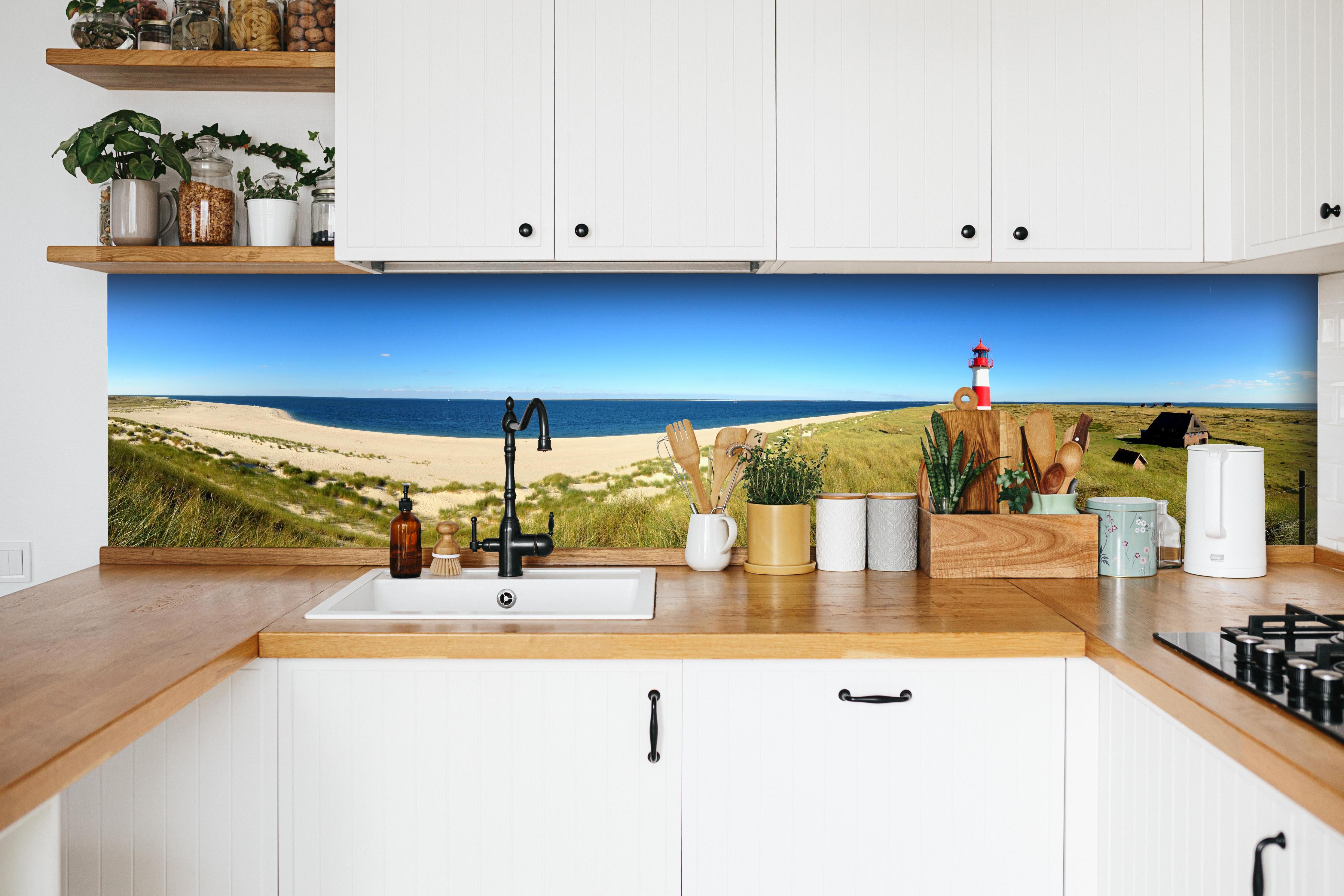 Küche - Leuchtender Leuchtturm an idyllischem Sandstrand hinter weißen Hochglanz-Küchenregalen und schwarzem Wasserhahn