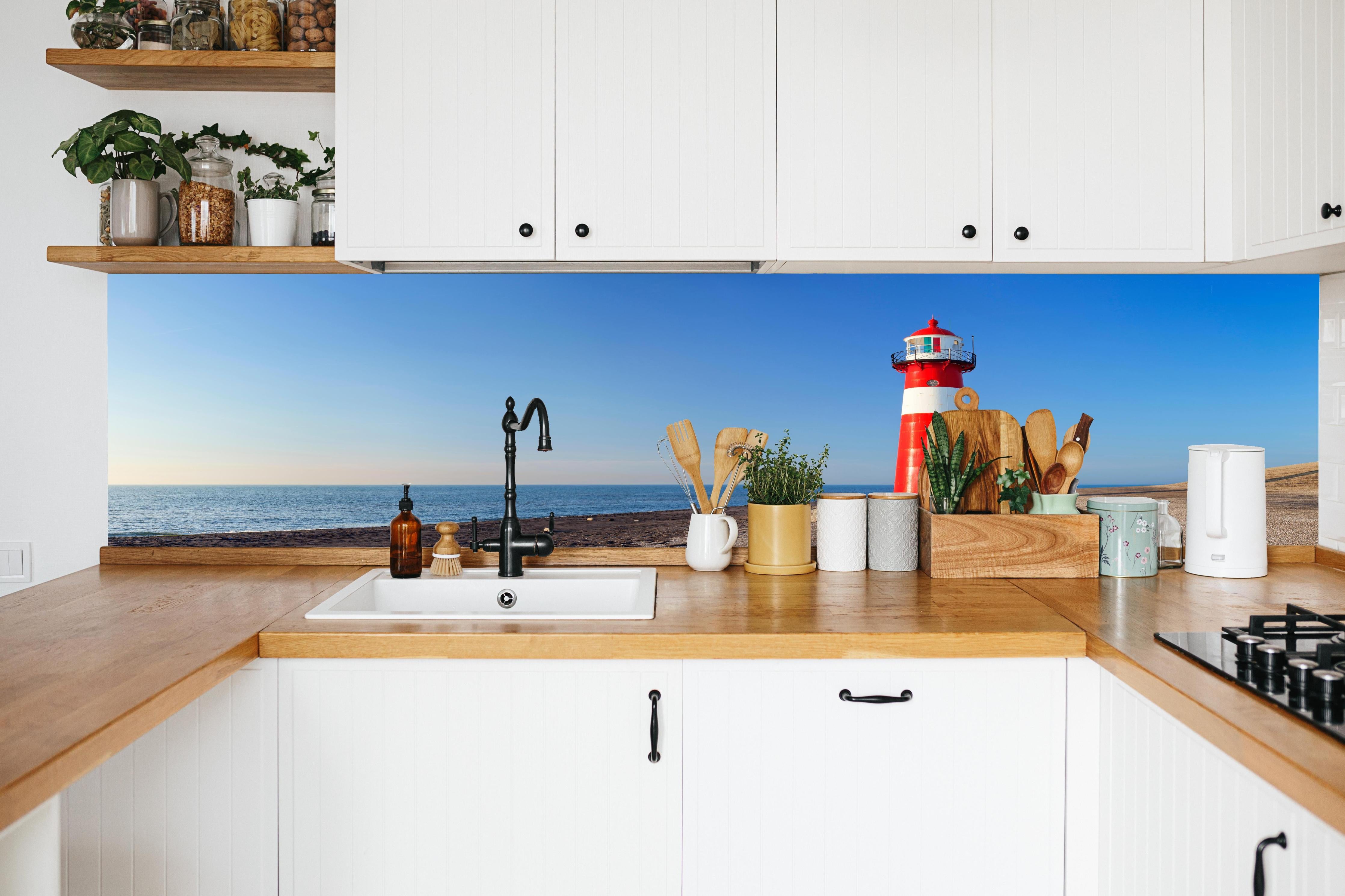 Küche - Leuchtturm in strahlendem Rot und Weiß vor weitem blauen Himmel hinter weißen Hochglanz-Küchenregalen und schwarzem Wasserhahn