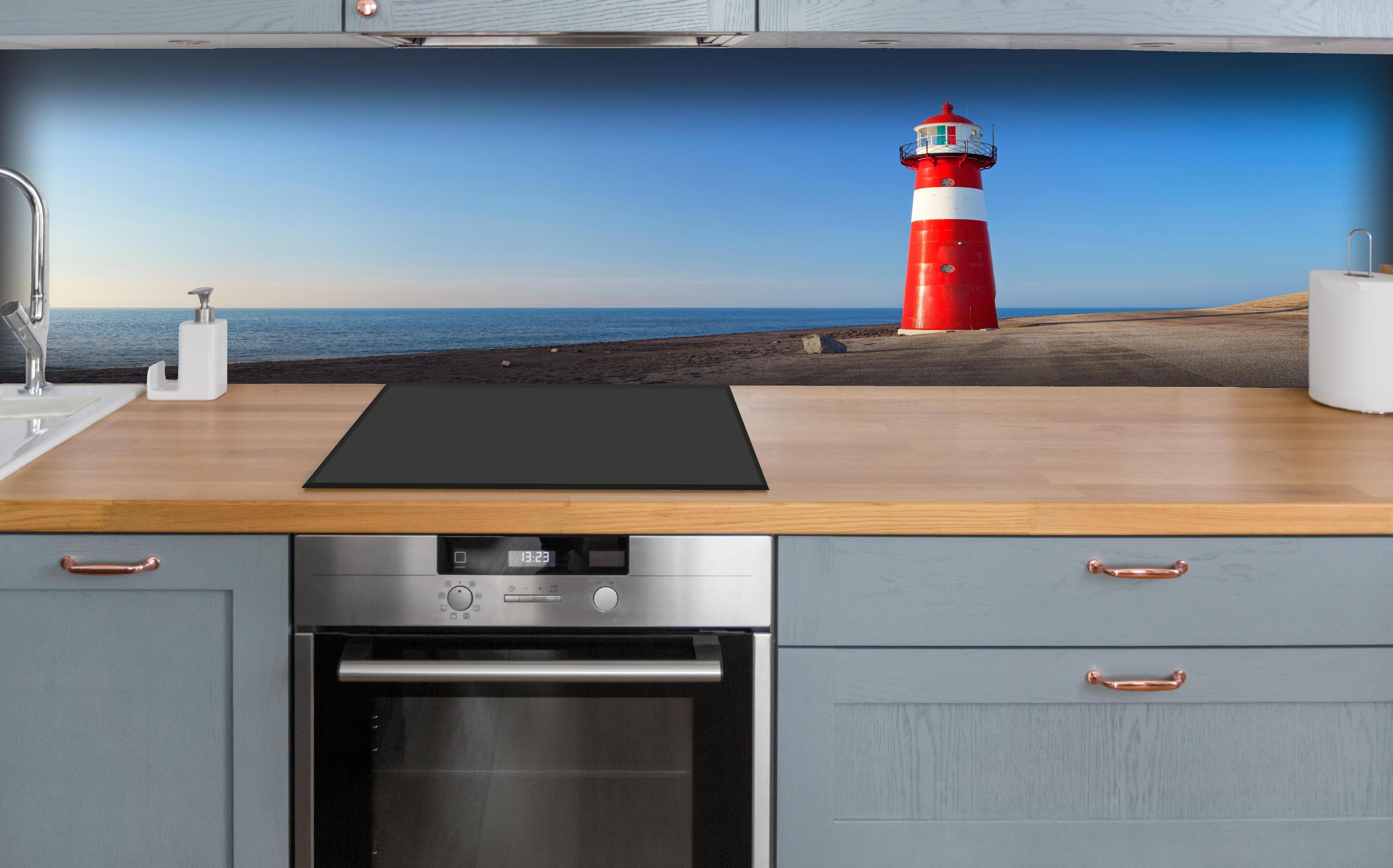 Küche - Leuchtturm in strahlendem Rot und Weiß vor weitem blauen Himmel hinter weißen Hochglanz-Küchenregalen und schwarzem Wasserhahn