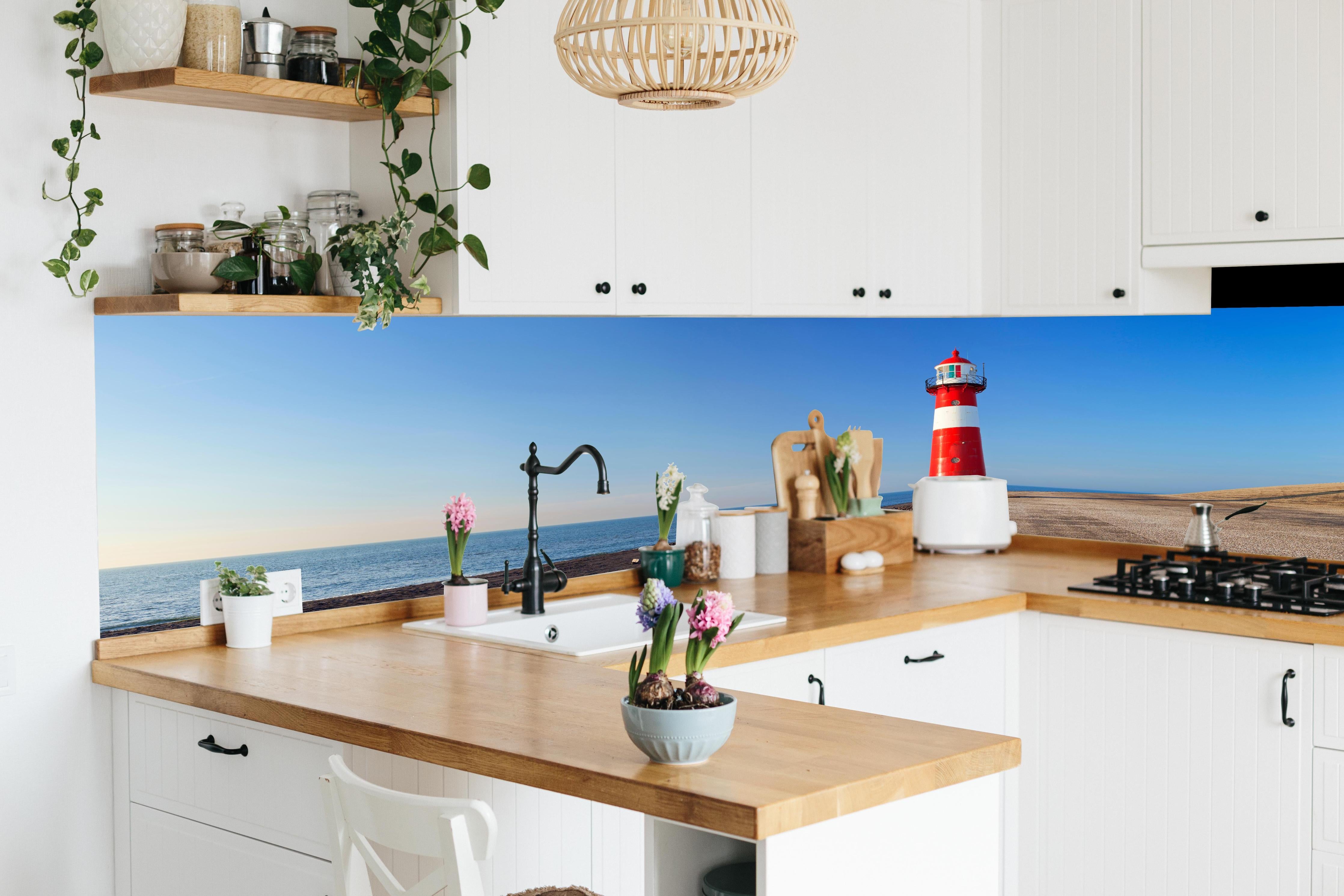 Küche - Leuchtturm in strahlendem Rot und Weiß vor weitem blauen Himmel hinter weißen Hochglanz-Küchenregalen und schwarzem Wasserhahn