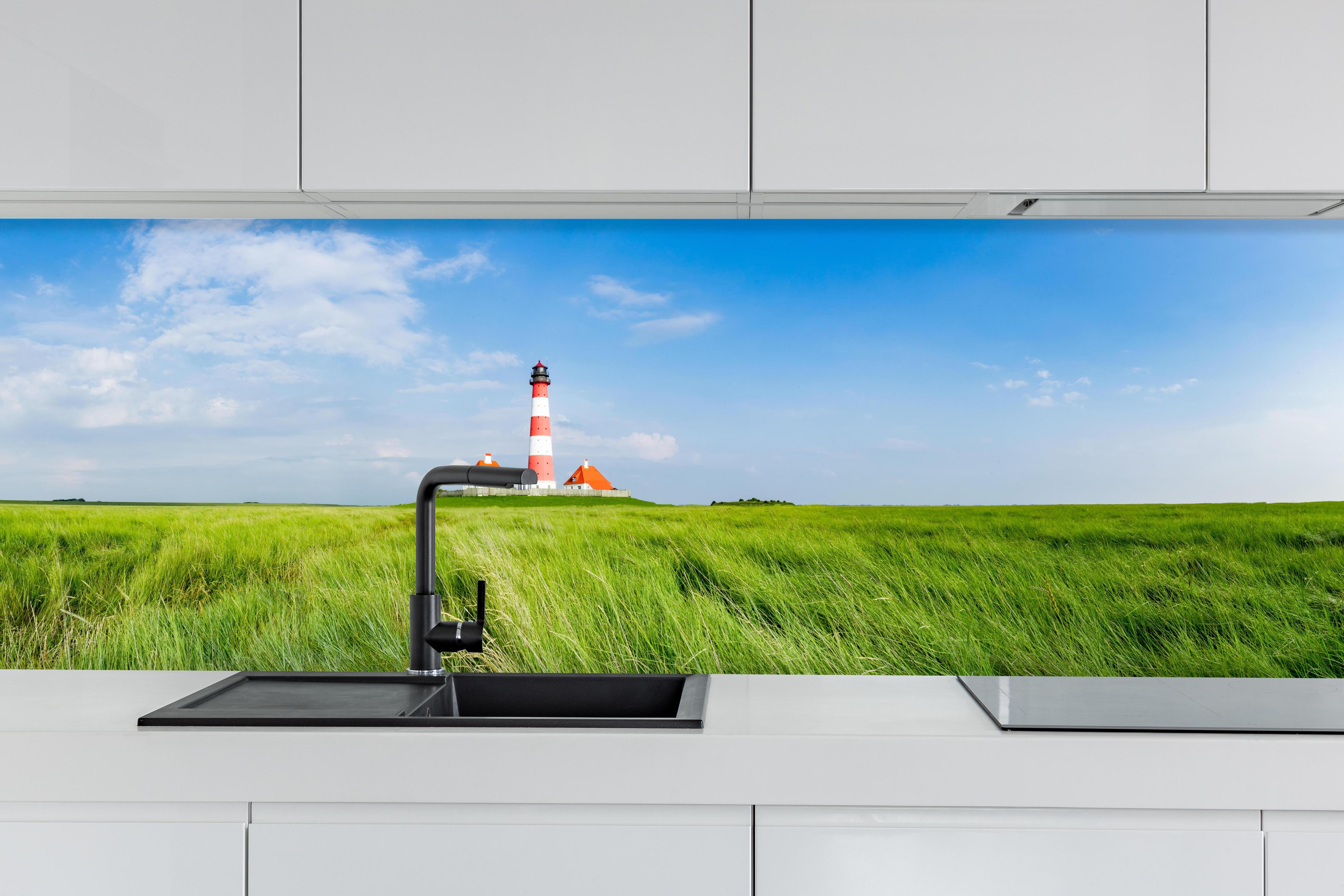 Küche - Leuchtturm vor herrlicher grüner Wiese unter klarem Himmel hinter weißen Hochglanz-Küchenregalen und schwarzem Wasserhahn