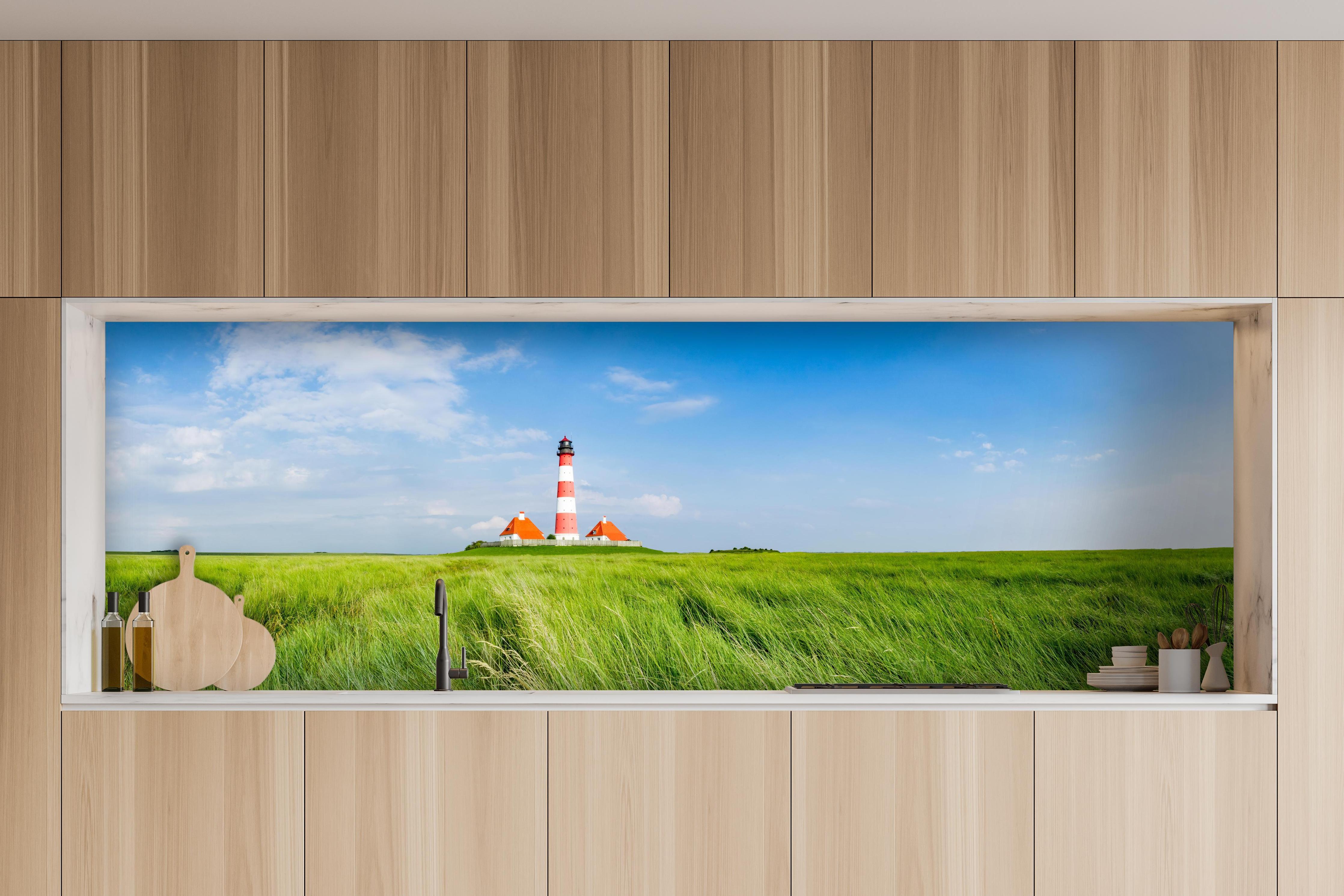 Küche - Leuchtturm vor herrlicher grüner Wiese unter klarem Himmel hinter weißen Hochglanz-Küchenregalen und schwarzem Wasserhahn