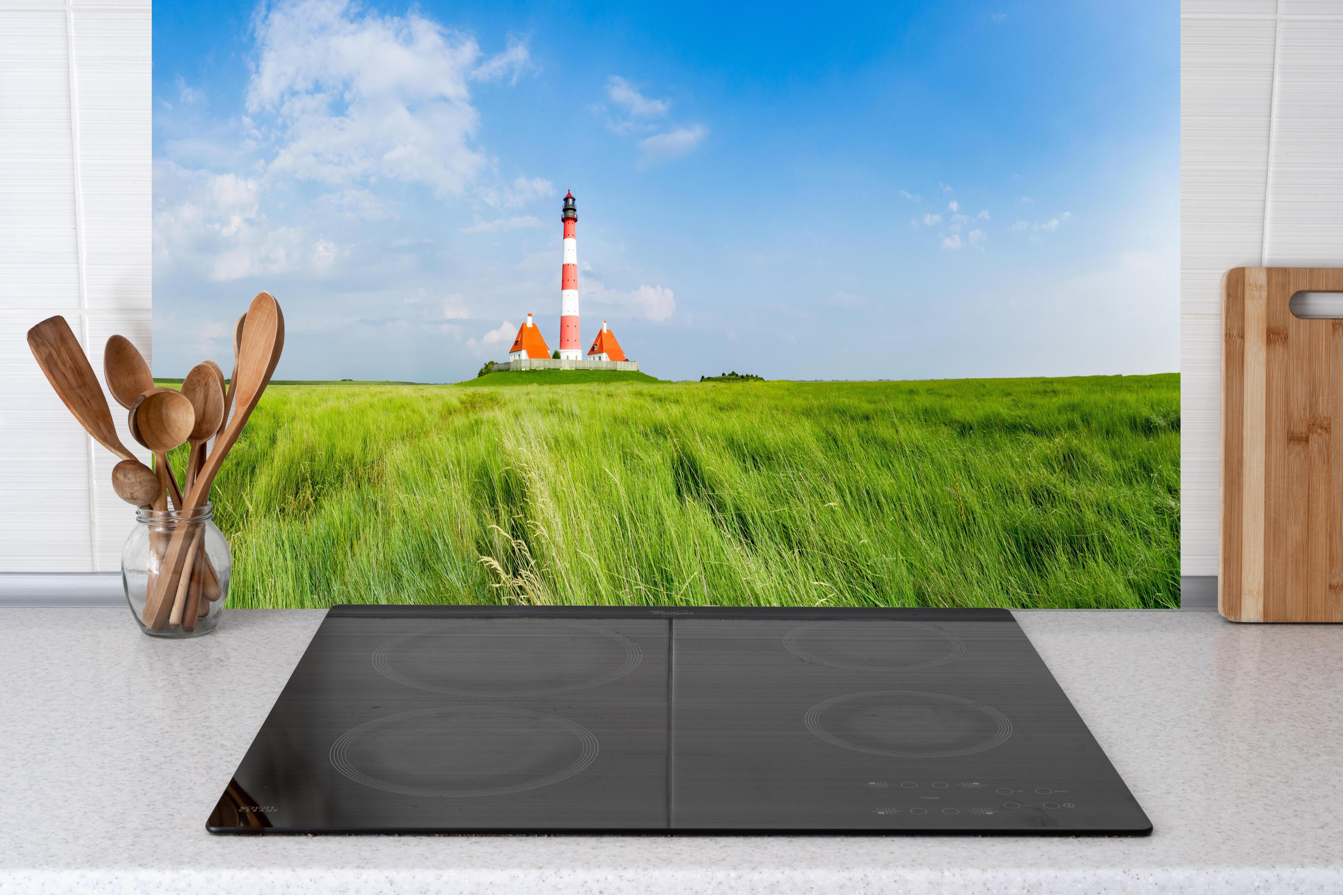 Küche - Leuchtturm vor herrlicher grüner Wiese unter klarem Himmel hinter weißen Hochglanz-Küchenregalen und schwarzem Wasserhahn