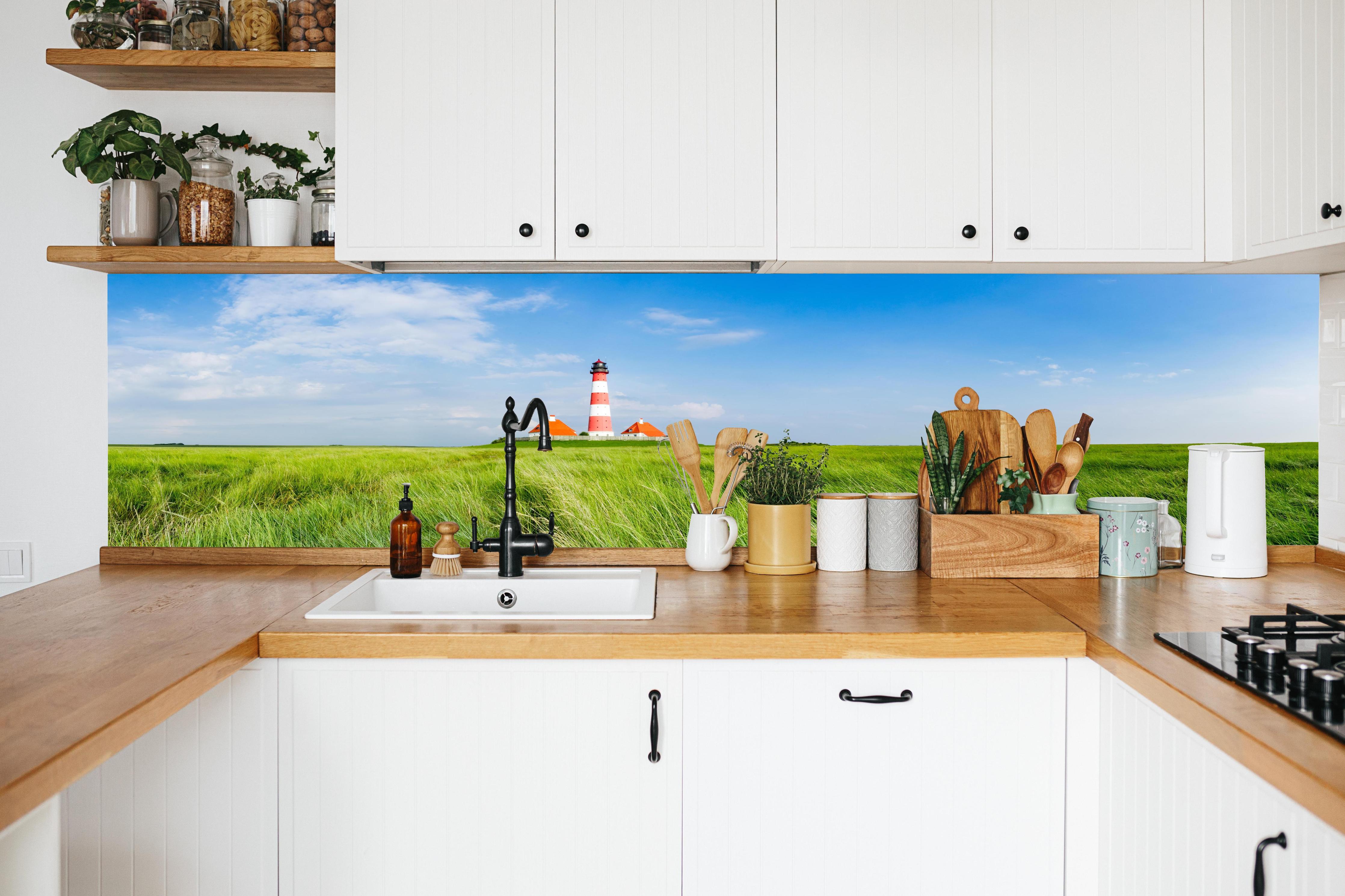 Küche - Leuchtturm vor herrlicher grüner Wiese unter klarem Himmel hinter weißen Hochglanz-Küchenregalen und schwarzem Wasserhahn