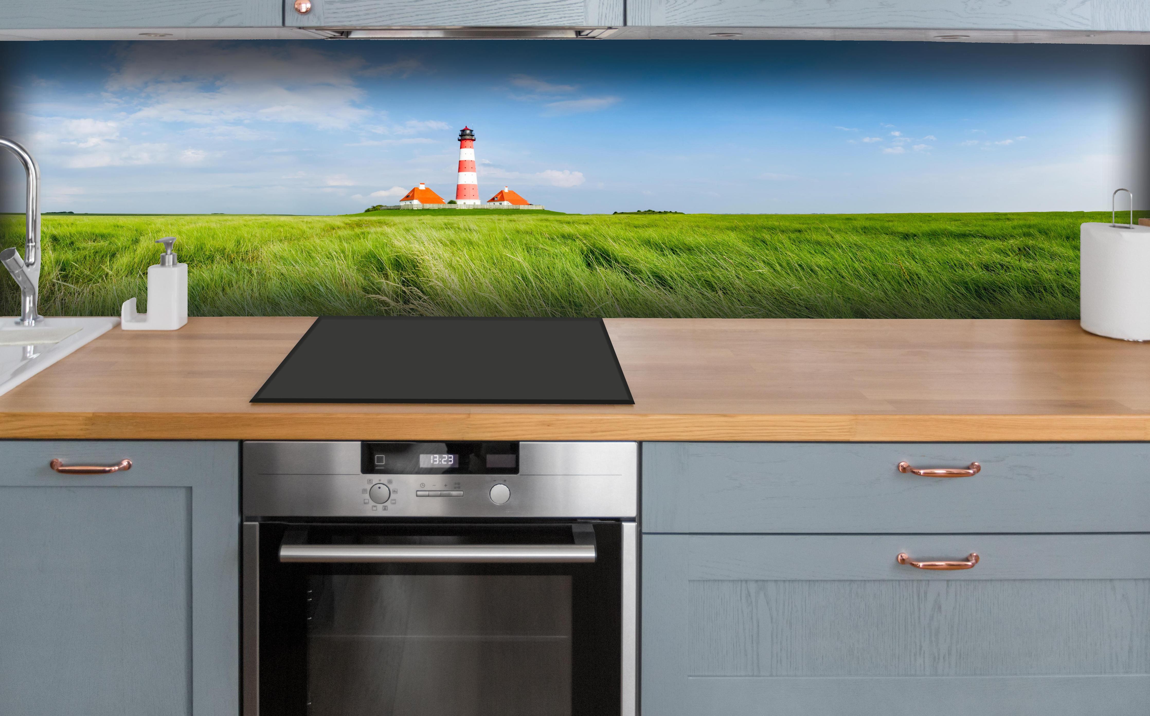Küche - Leuchtturm vor herrlicher grüner Wiese unter klarem Himmel hinter weißen Hochglanz-Küchenregalen und schwarzem Wasserhahn