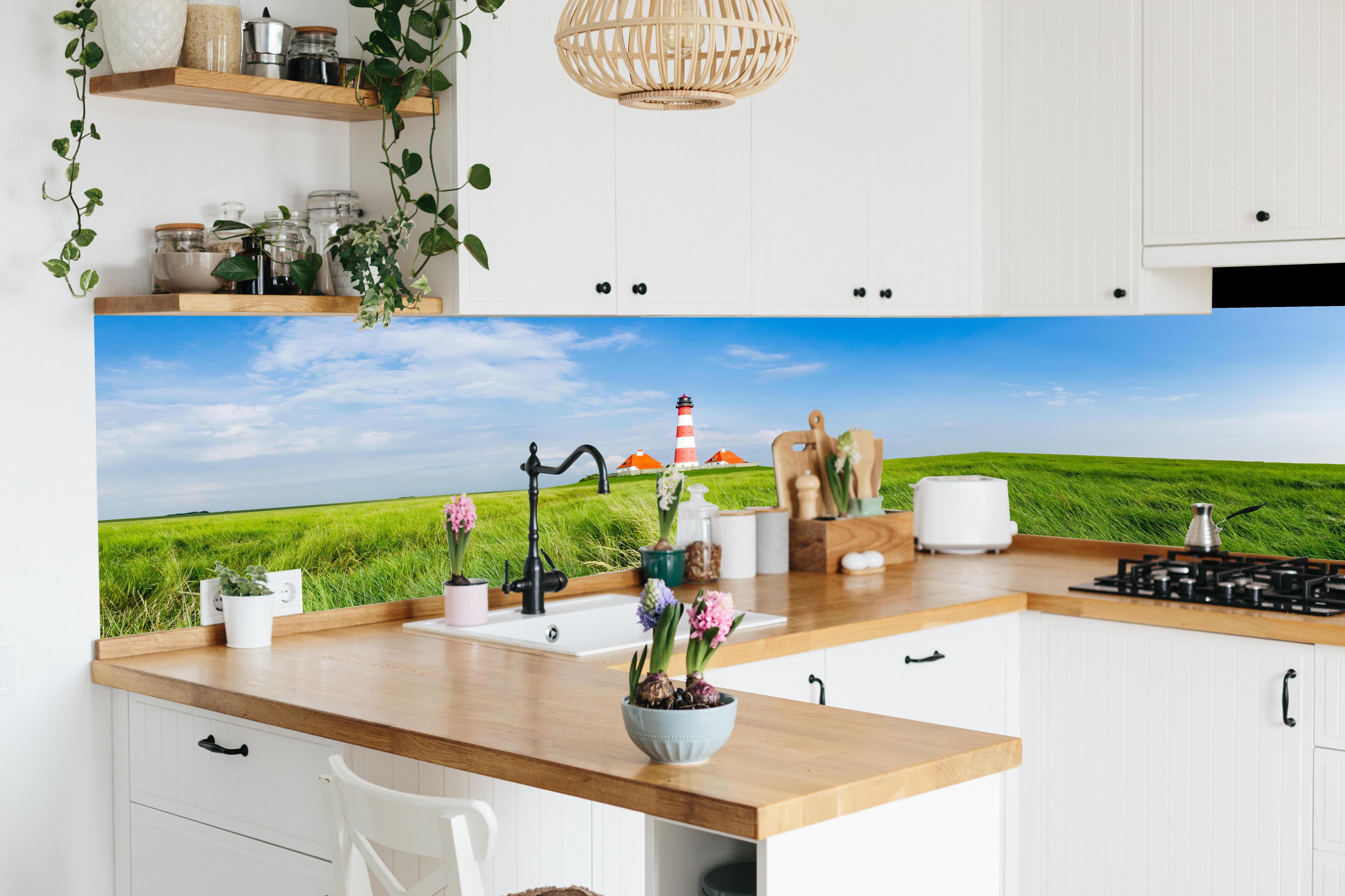 Küche - Leuchtturm vor herrlicher grüner Wiese unter klarem Himmel hinter weißen Hochglanz-Küchenregalen und schwarzem Wasserhahn